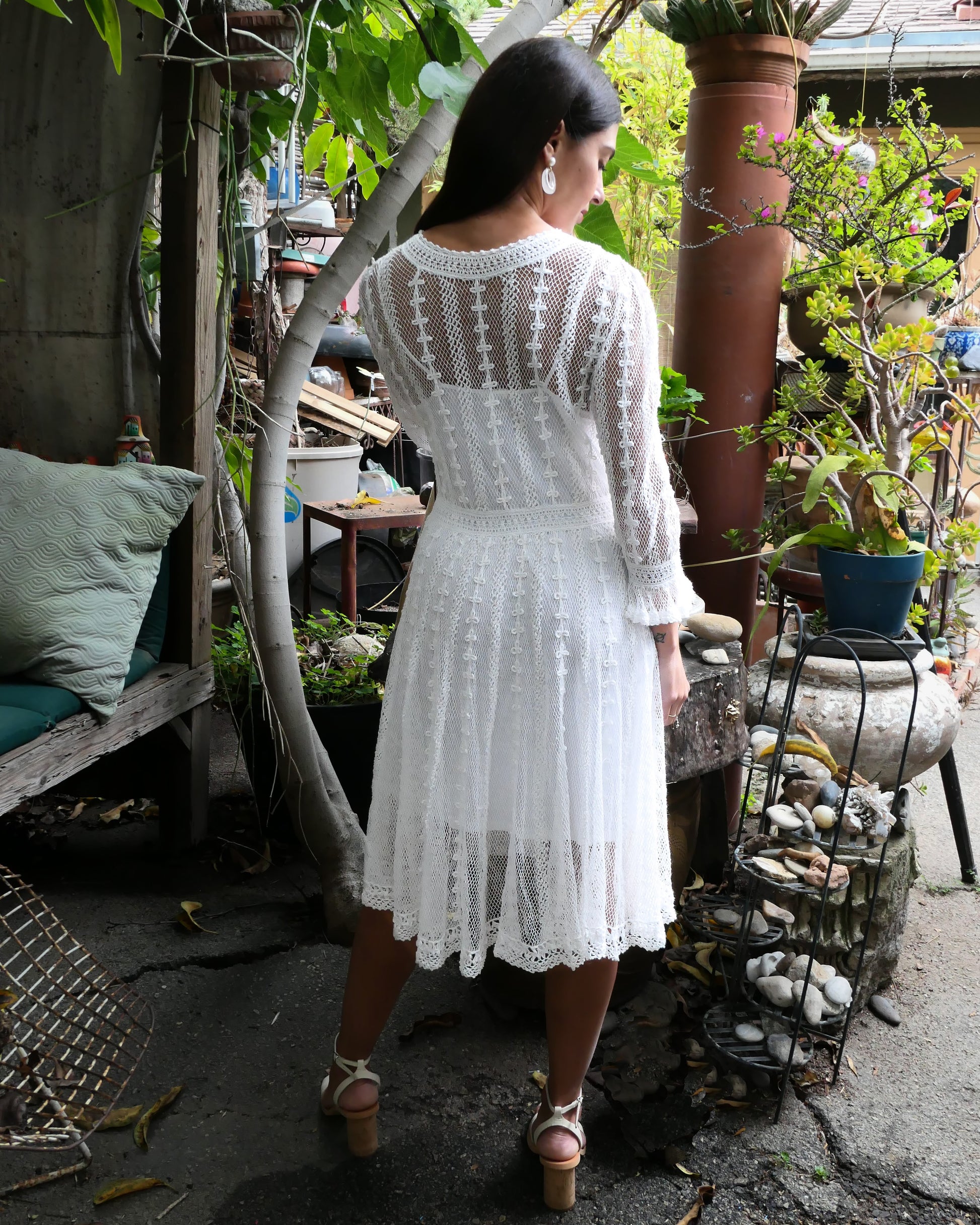 Back of dress. Lim's Vintage original crochet cottage core style dress. This dreamy midi length dress can be worn buttoned up the front or back and is made with very fine threads, making the dress refined and sheer. Detailed crochet trim is used for the waist, hemline, and 3/4 length ruffled sleeves. Wear it with a natural or pink colored slip or bandeau bra and bikini shorts and a pair of ankle or knee-high boots to complete the look.