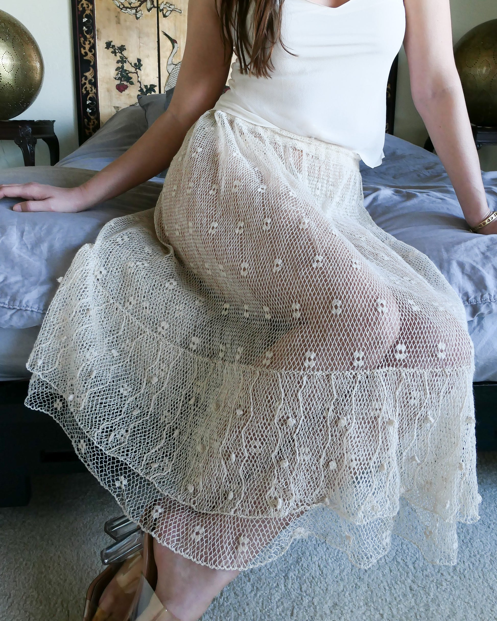 Closeup of skirt. Like the delicate petals of the California Poppy, this skirt wafts and floats like a gentle summer breeze. Made with a delicate fishnet crochet, dotted with mini florettes, and accented with a two-tiered ruffle hem, this dress is sure to sweep you off your feet! Comes with a comfortable fitting elastic waistband that rests easily on the waist. Great as a beach coverup with a pair of wedgy sandals, a cute straw hat, and a mojito in hand.  Size: Fits small to medium