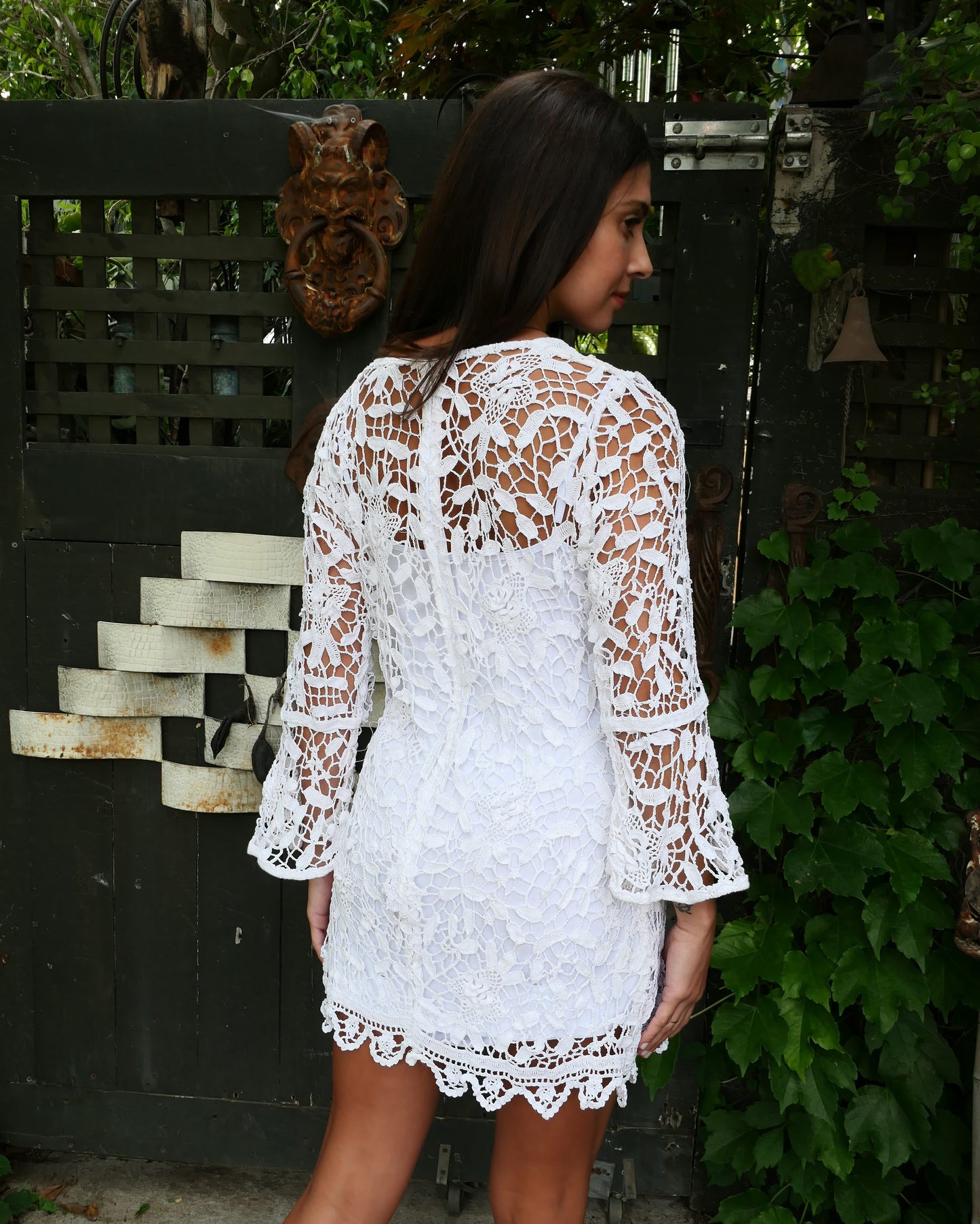 Back view of dress. A flattering, versatile bell sleeve mini dress using our Lim's Vintage hand crocheted floral and leaf motif fabric. The dress zips up the back and is slightly fitted at the waist, yet has enough room and give to compliment most body types. Looks great as a beach coverup or over a white slip dress. Color: White