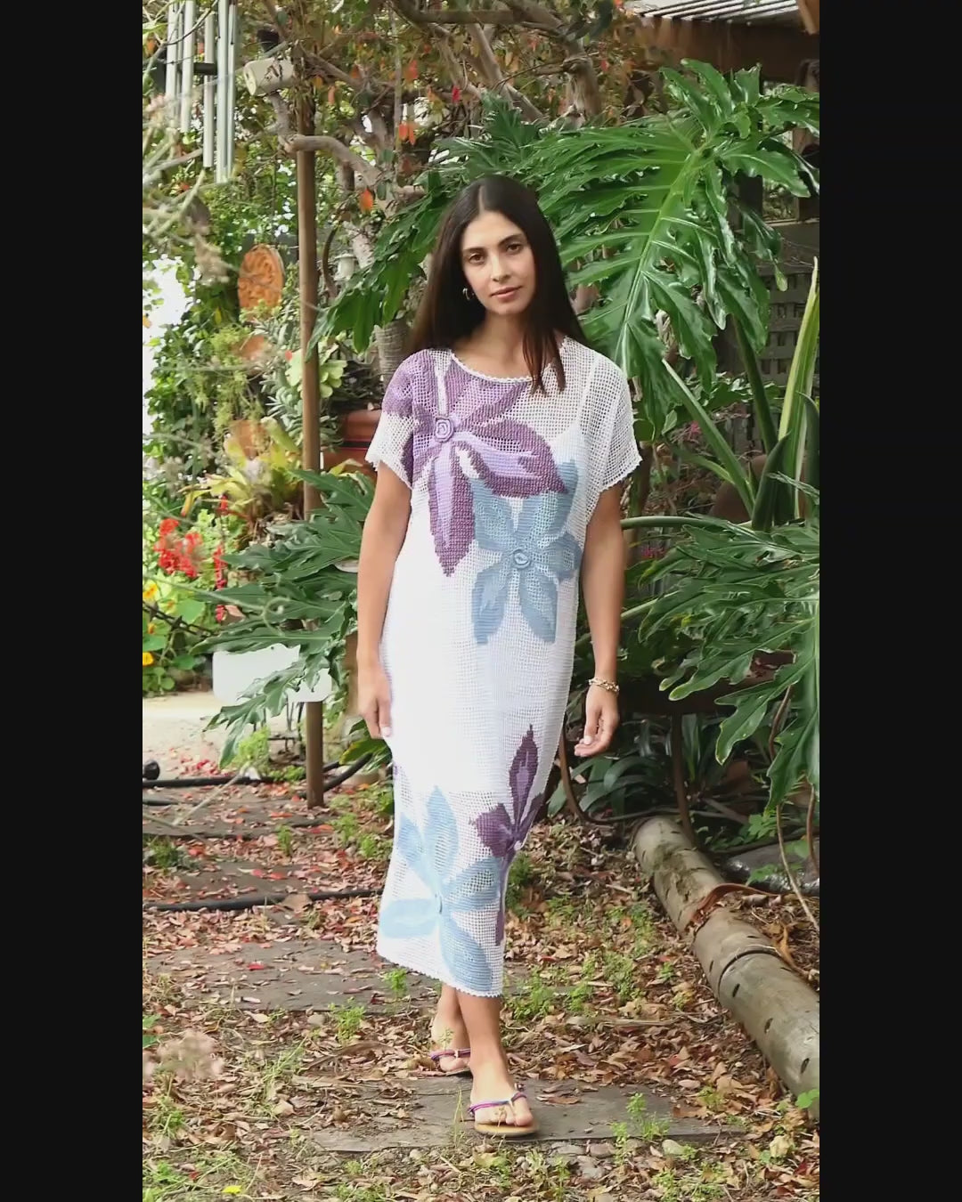 Video of model in white mumu dress with purple and blue big, bold flowers.  A hand crocheted, island inspired mumu dress with bold, beautiful flowers set against a simple crochet backdrop. This easy oversized pullover dress is great for those days at the beach. Wear it over a bathing suit or lightweight slip dress, a sun hat, and sandals for an effortless boho chic vibe. 