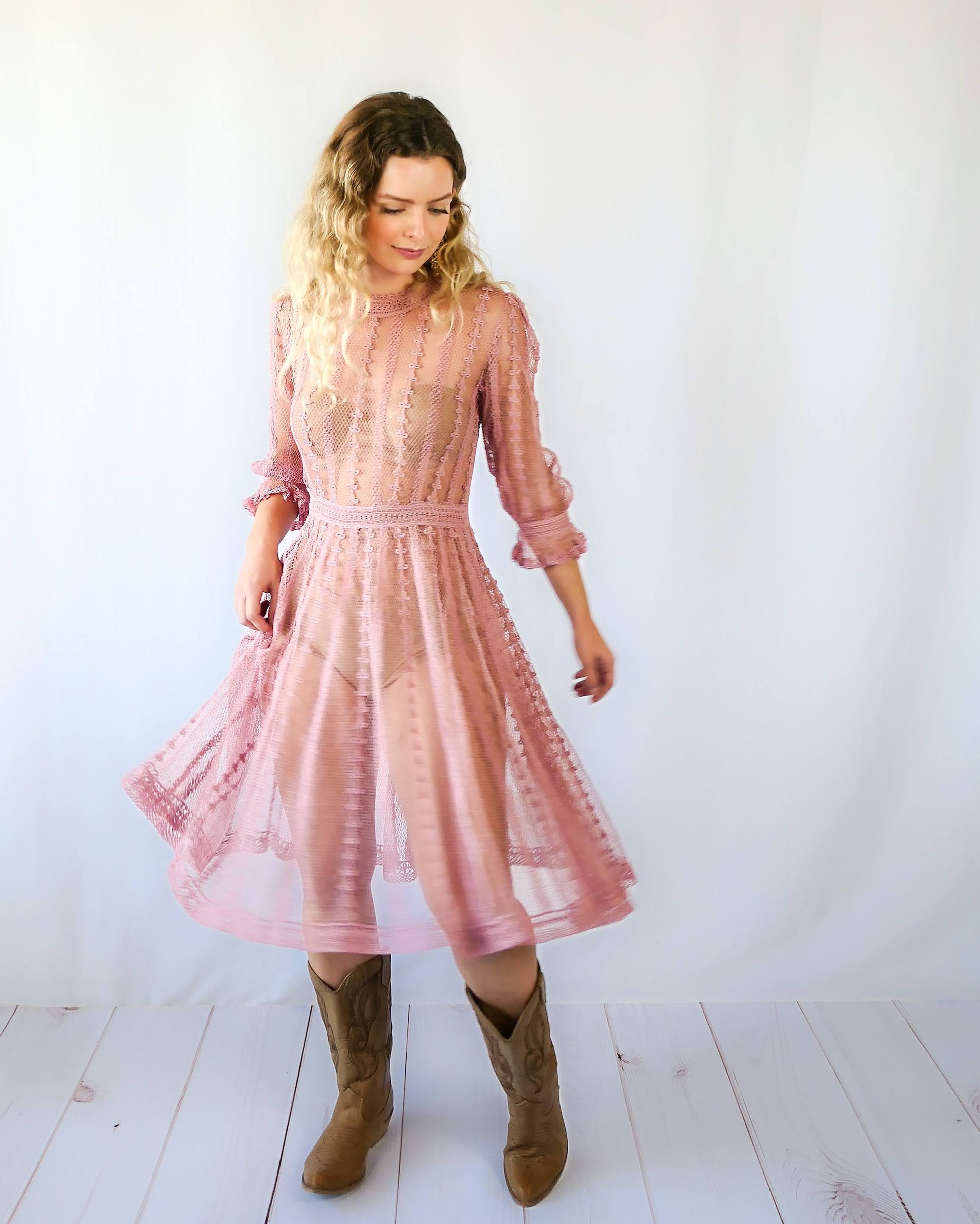 Picture of Lim's Vintage midi length crochet dress in muted rose color. The model is twirling around. Fitted waist, flares out towards the hem. Ruffle at the bottom of the sleeves. Made with fine cotton yarns to create a sheer look.