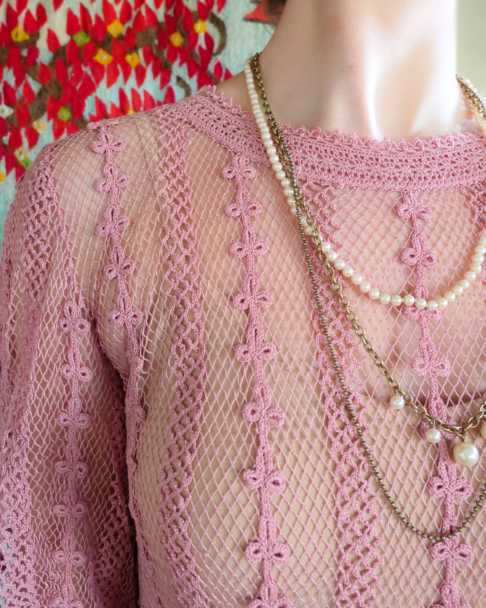 Closeup view of round neckline with detailed crochet trim.  One of our original Lim's crochet maxi dresses in a muted rose color from the 1980's. A darling of a piece and sure to turn heads, this dress was intricately hand crocheted using very fine cotton threads.   3/4 length sleeves, round collar, with ruffles at the wrist.  Model is wearing a natural colored slip underneath. 