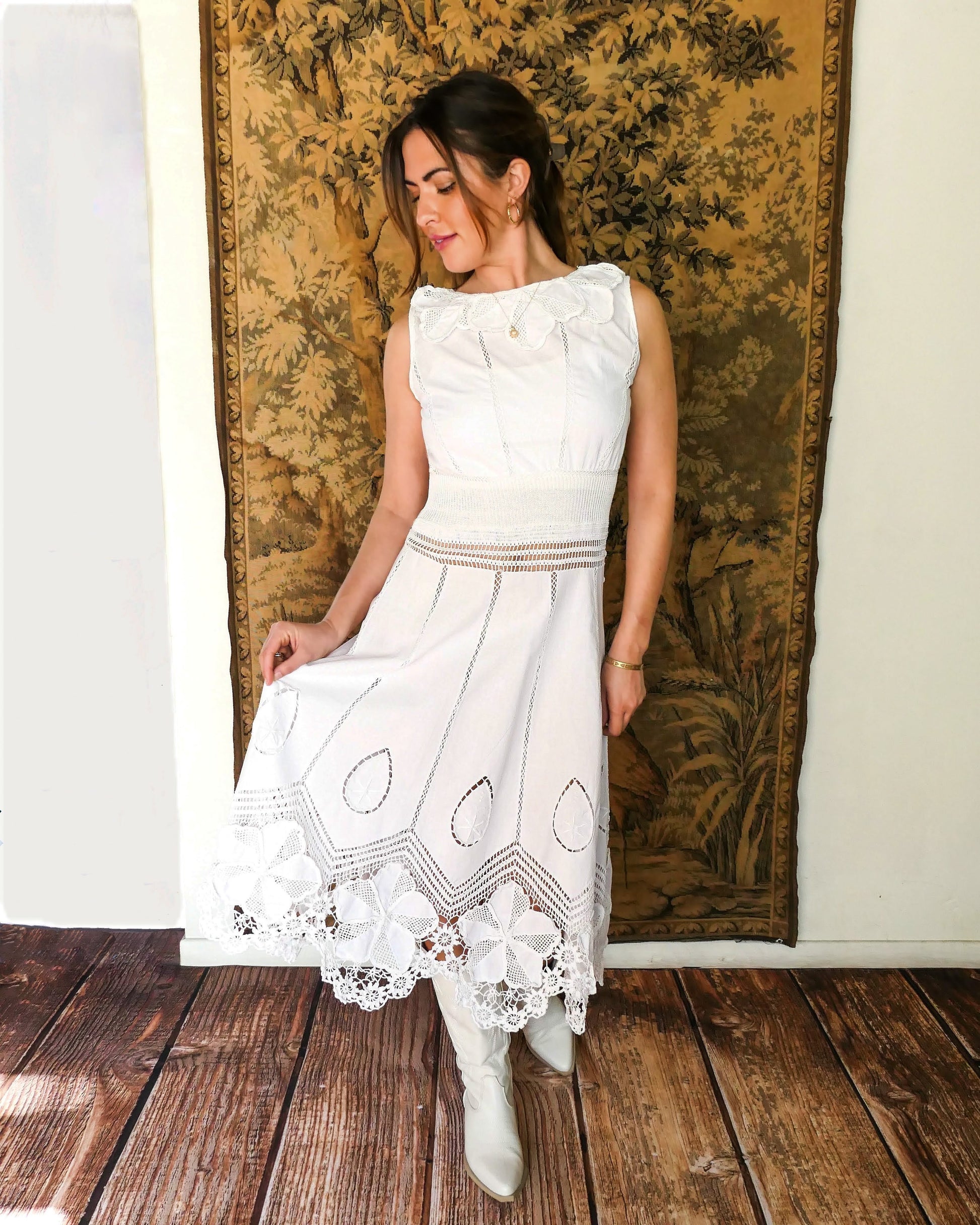 A white cotton midi dress with whimsical crochet and embroidered flowers at the hem and collar, and teardrop shaped eyelet detail on the skirt. Stretchable ribbed knit fabric around the waist adds contour to the dress.  By Lim's Vintage.