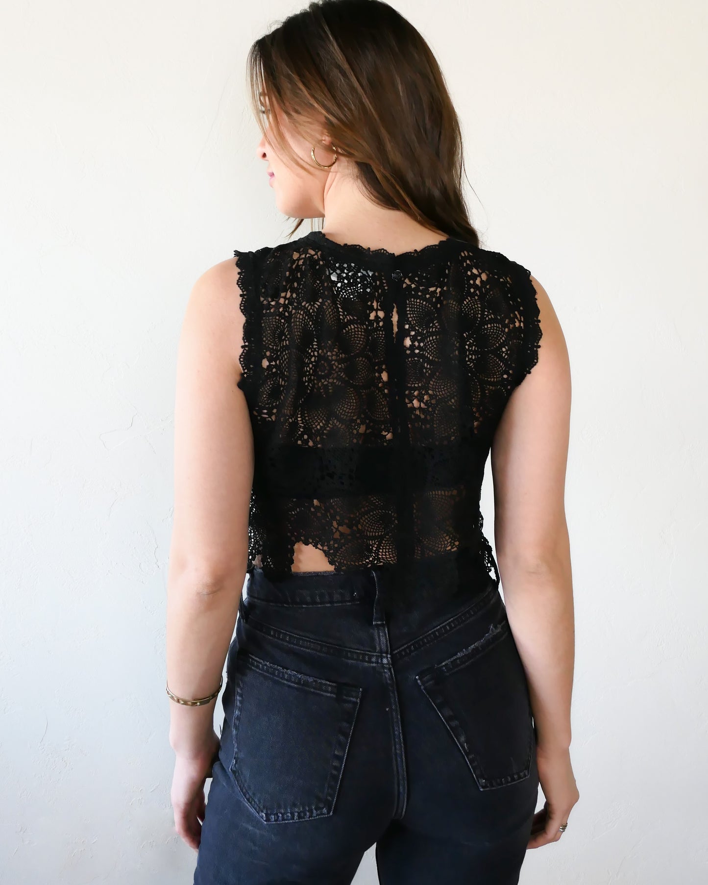 Back view. An ultra casual, hip, and boho-chic crop tank top made with interconnected flower doilies reminiscent of the white lotus, which symbolizes peace, tranquility, and calmness.  Lace trim at the collar and sleeve.  Model is wearing black colored top by Lim's Vintage.