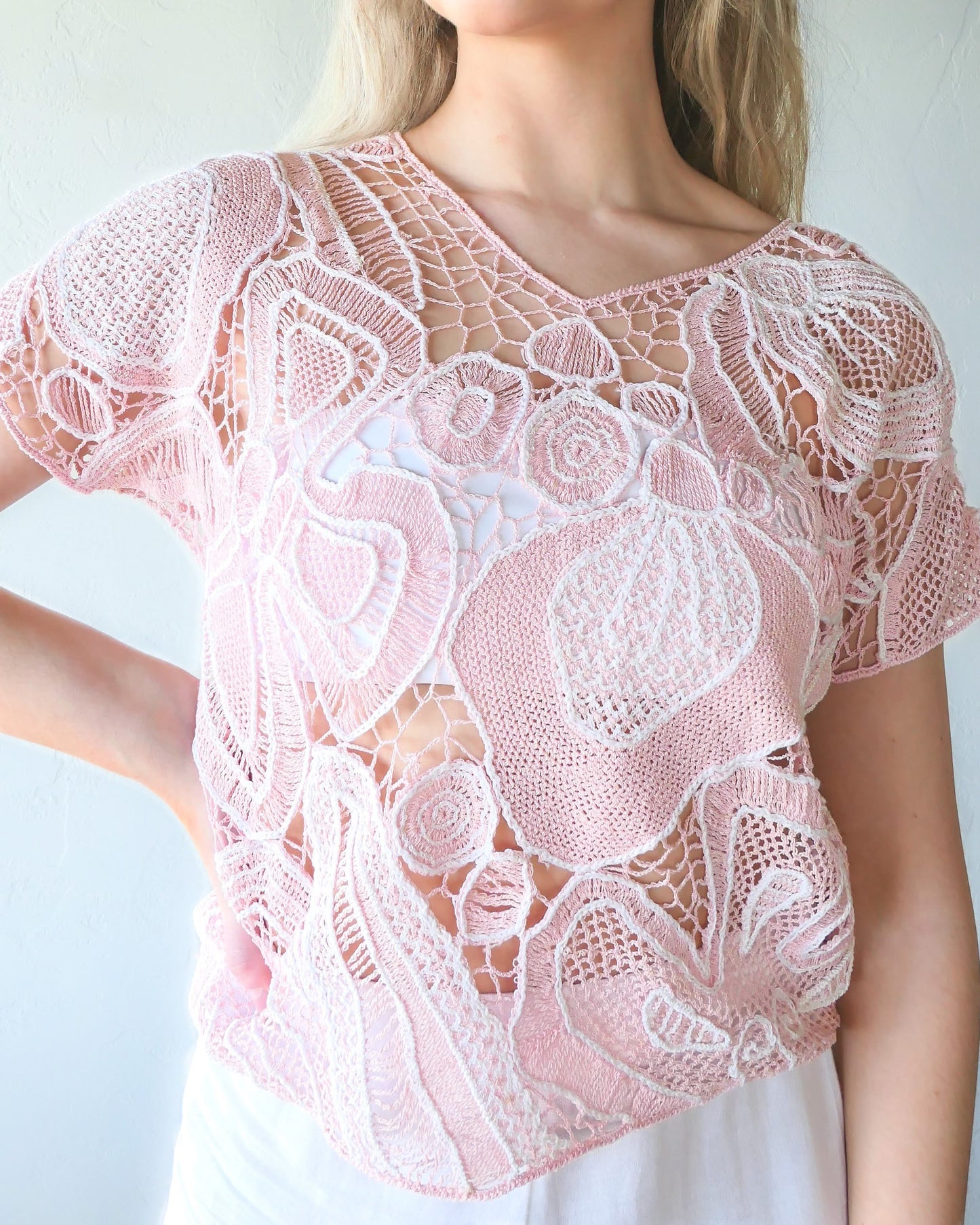 Closeup front view of girl wearing a crochet top with abstract flora design in colors of cotton candy pink and white. Lim's Vintage original crochet top from the 1980s.