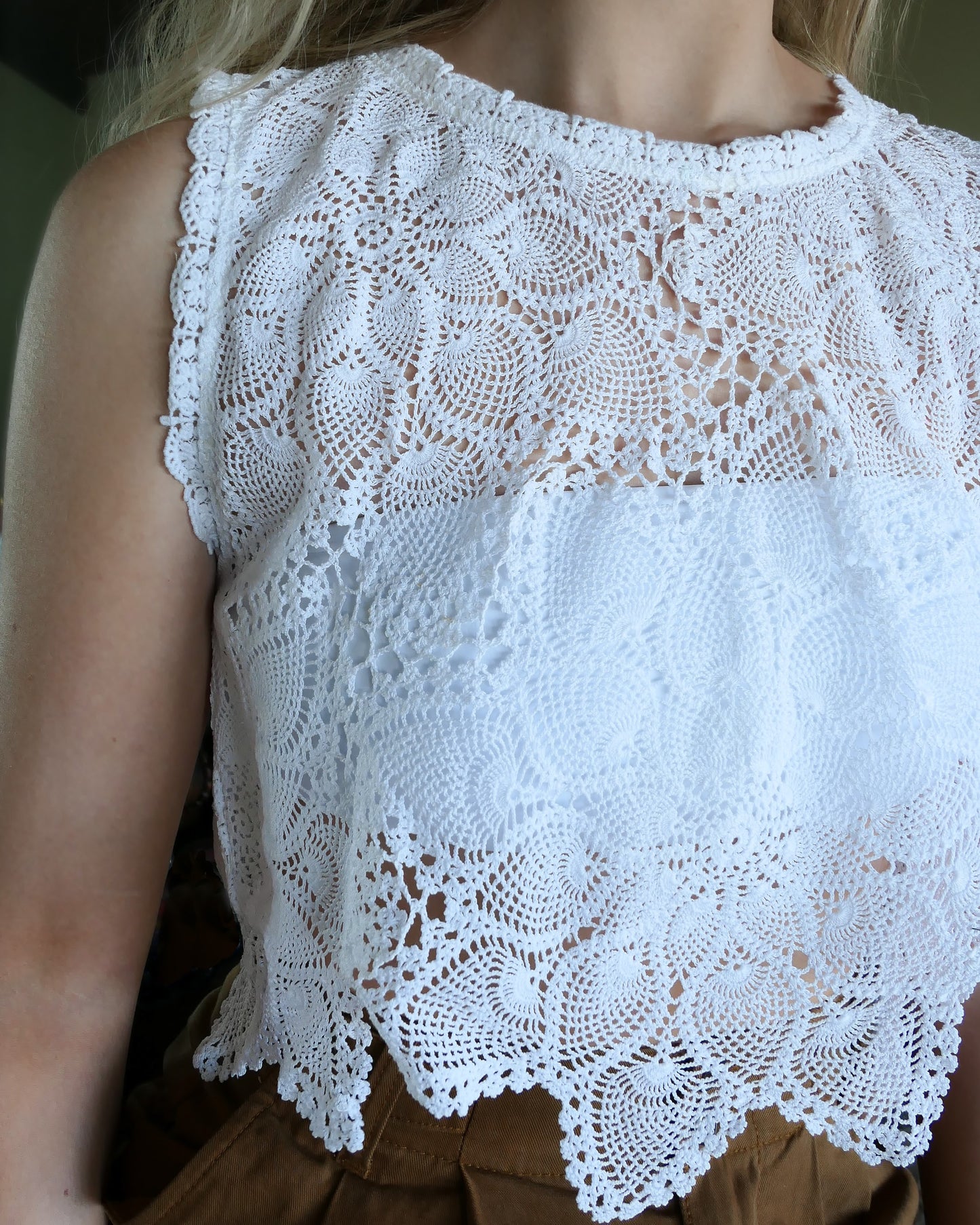 An ultra casual, hip, and boho-chic crop tank top made with interconnected flower doilies reminiscent of the white lotus, which symbolizes peace, tranquility, and calmness. Lace trim at the collar and sleeve. Model is wearing a white colored crochet Lim's Vintage top.