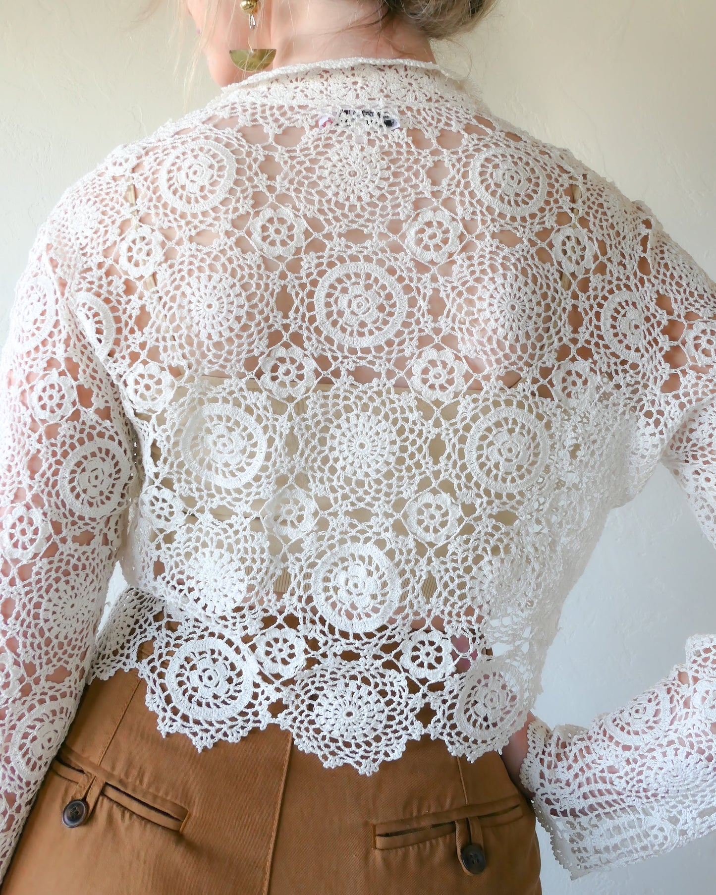 Back view of Lim's Vintage crochet cropped cardigan in ivory. A versatile and boho chic hand crocheted cropped cardigan sweater in Ivory with a unique, repeating kaleidoscope-like floral pattern throughout. Dress it down with a pair of jeans and sandals, or dress it up with neutral colored wide leg pants, heels, and a pair of vintage dangly earrings.  Size: Fits Small to Medium