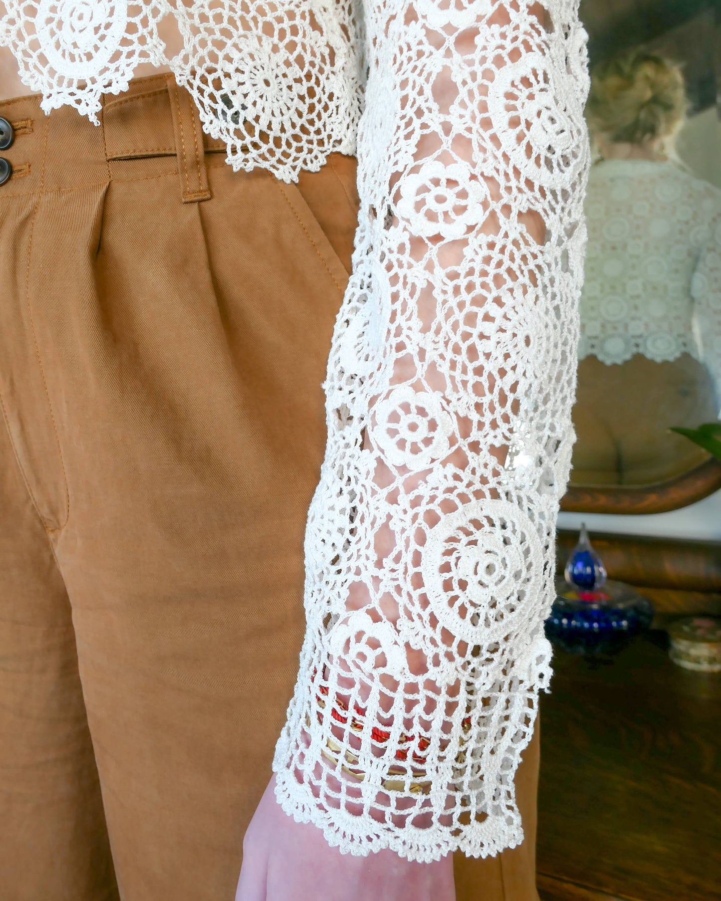 Closeup of the sleeve. Hand crocheted Lim's cardigan.  A versatile and boho chic hand crocheted cropped cardigan sweater in Ivory with a unique, repeating kaleidoscope-like floral pattern throughout. Dress it down with a pair of jeans and sandals, or dress it up with neutral colored wide leg pants, heels, and a pair of vintage dangly earrings.  Size: Fits Small to Medium