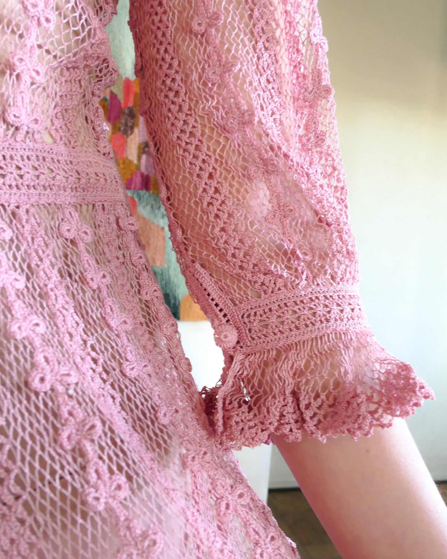 Closeup of ruffled sleeve with button.  One of our original Lim's crochet maxi dresses in a muted rose color from the 1980's. A darling of a piece and sure to turn heads, this dress was intricately hand crocheted using very fine cotton threads.   3/4 length sleeves, round collar, with ruffles at the wrist.  Model is wearing a natural colored slip underneath. 