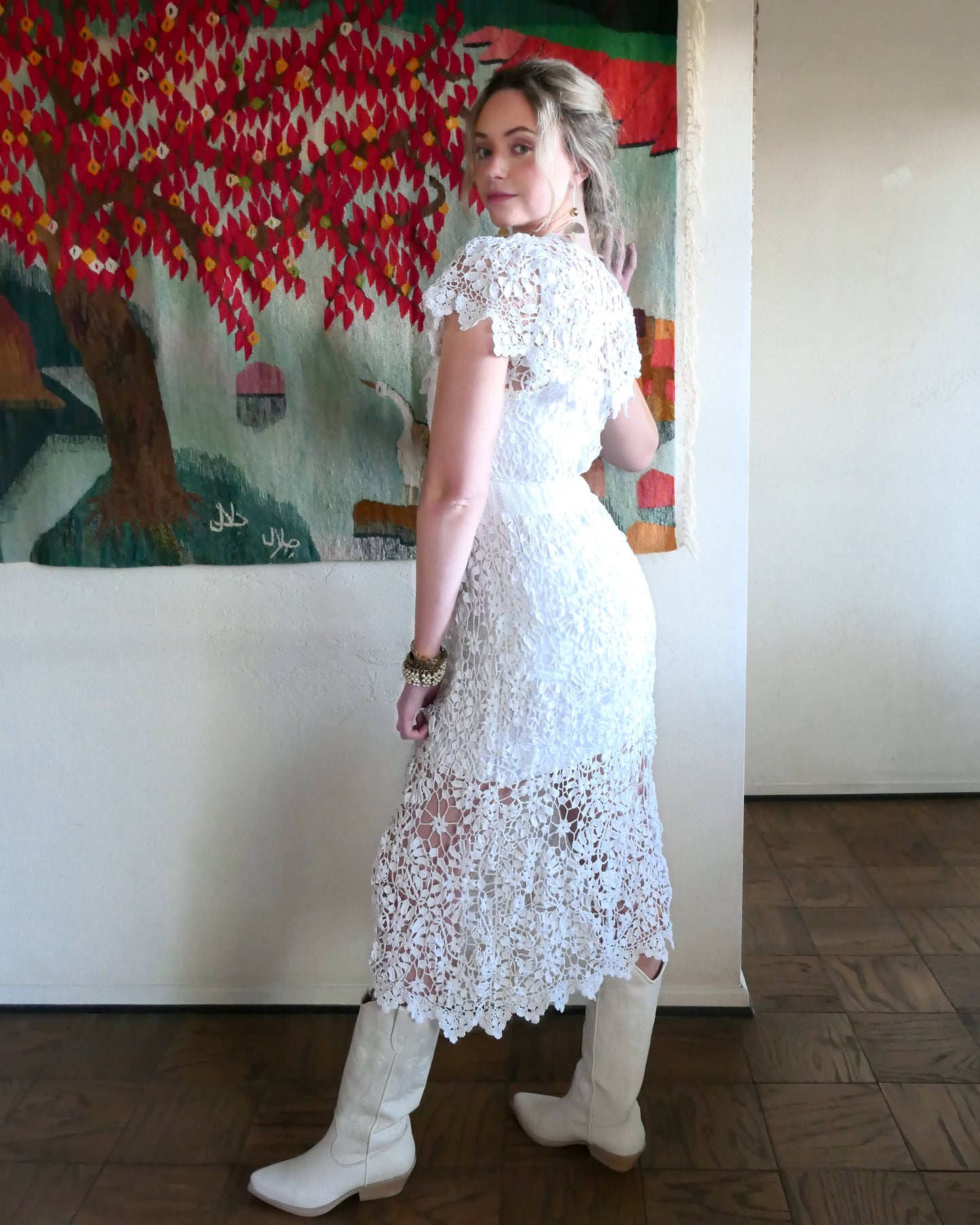 A romantic white crochet midi dress with a floral and leaf pattern, comfortable elastic waistband, and a flattering neck and shoulder design. Perfect as a vintage wedding dress or a special occasion! Wear with a white slip and heels for a refined, feminine look, or pair with boots for a more casual outing.