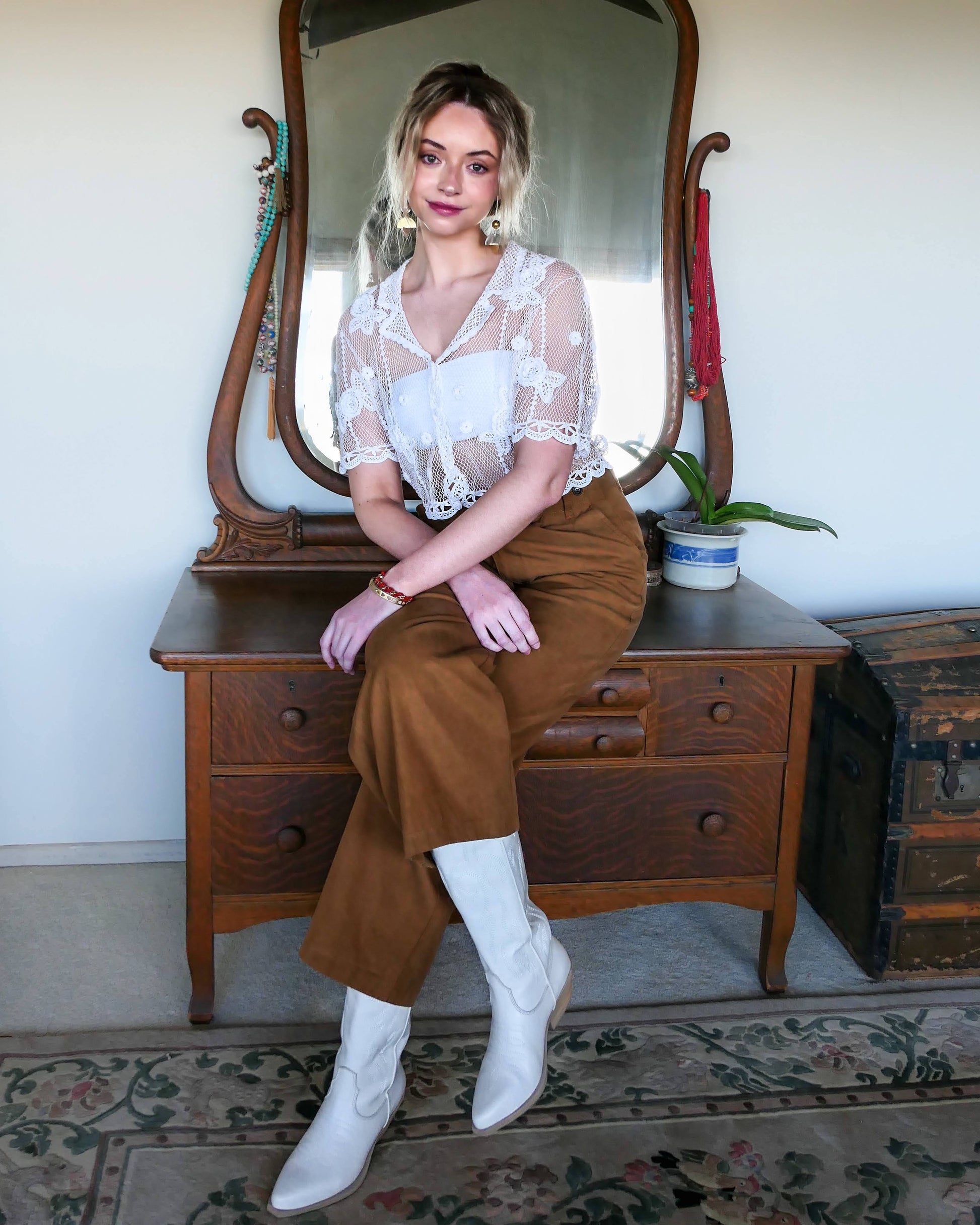 Add a romantic twist to your wardrobe with this Lim' Vintage original 1990s hand crocheted short sleeve cardigan with a carnation flower motif and scallopped hem at the sleeves and waist.  The cardigan is stretchable and fits a range of sizes.  In this photo, the model is wearing the white crochet top over a white bralette, with a pair of mustard colored flare pants and white cowboy boots.  