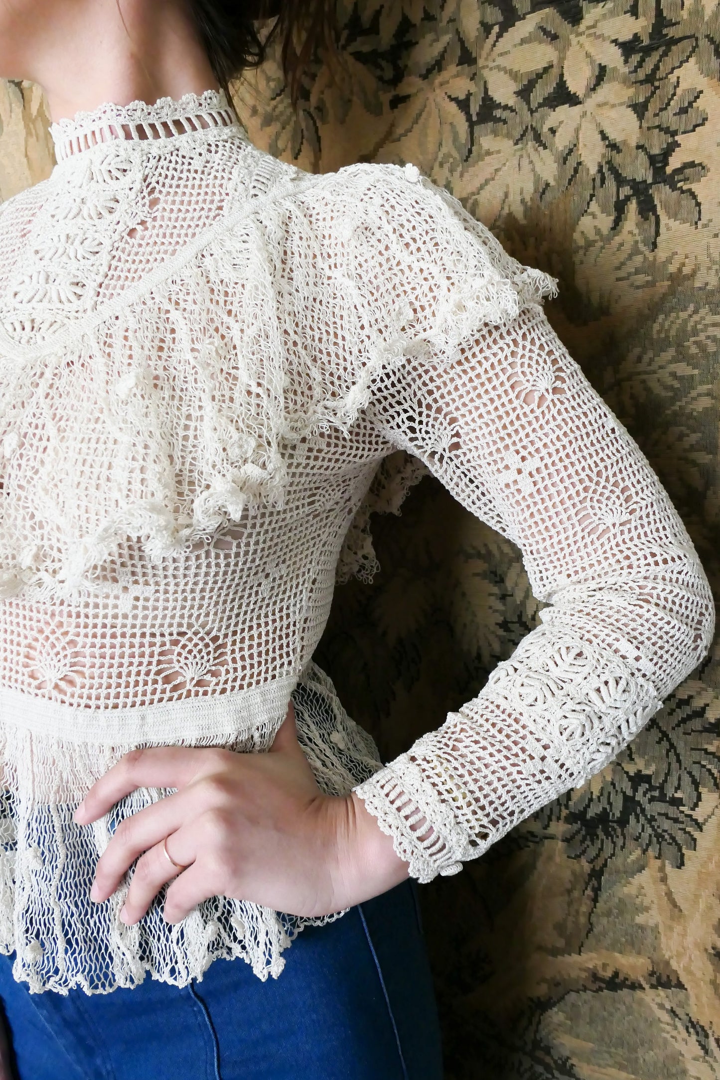 Closeup view of Lim's crochet Victorian style top with ruffles.  Detailed crochet work around the forearm and sleeve hem. Natural color. 