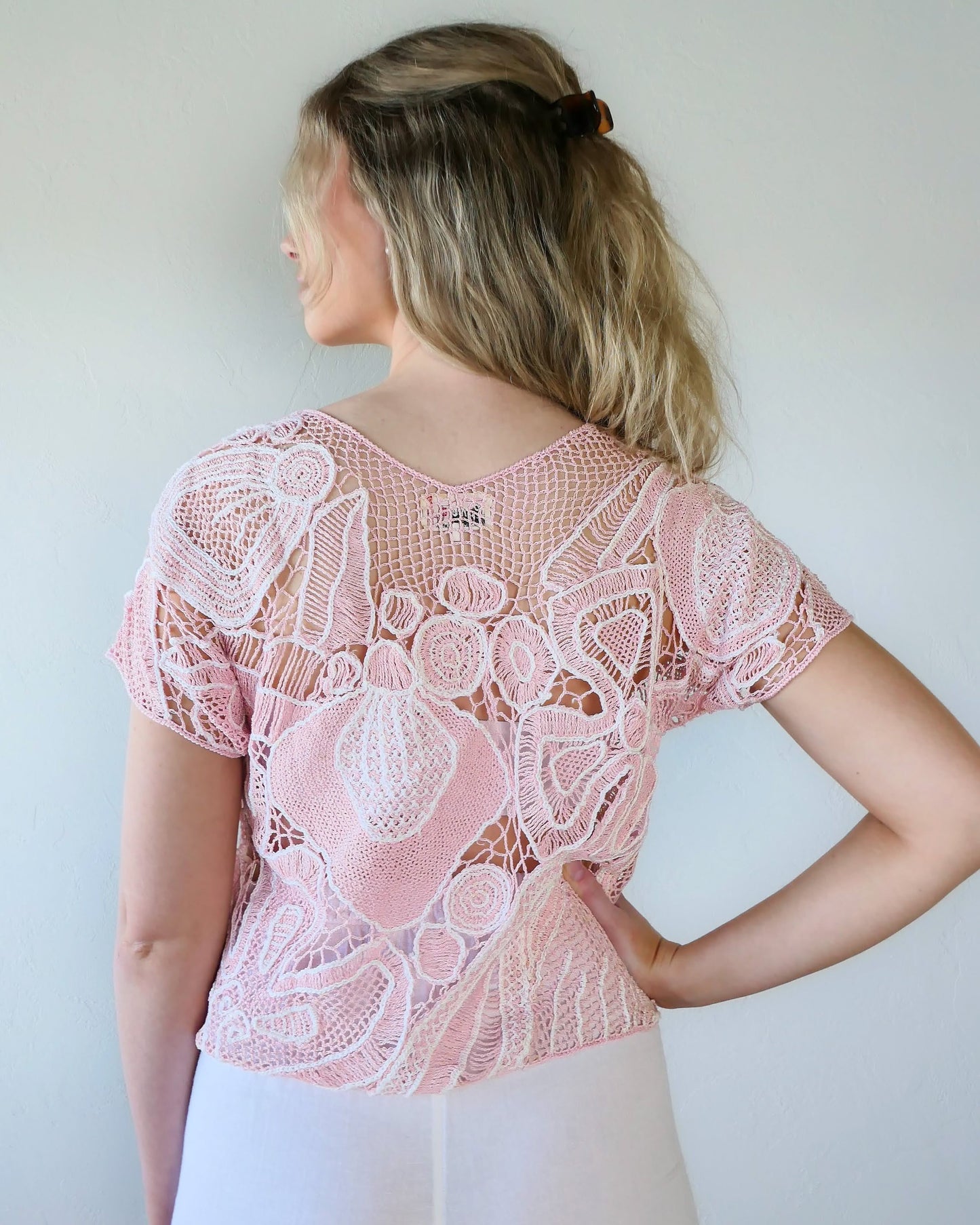 Back of view of girl wearing a crochet top with abstract flora design in colors of cotton candy pink and white. Lim's Vintage original crochet top from the 1980s.