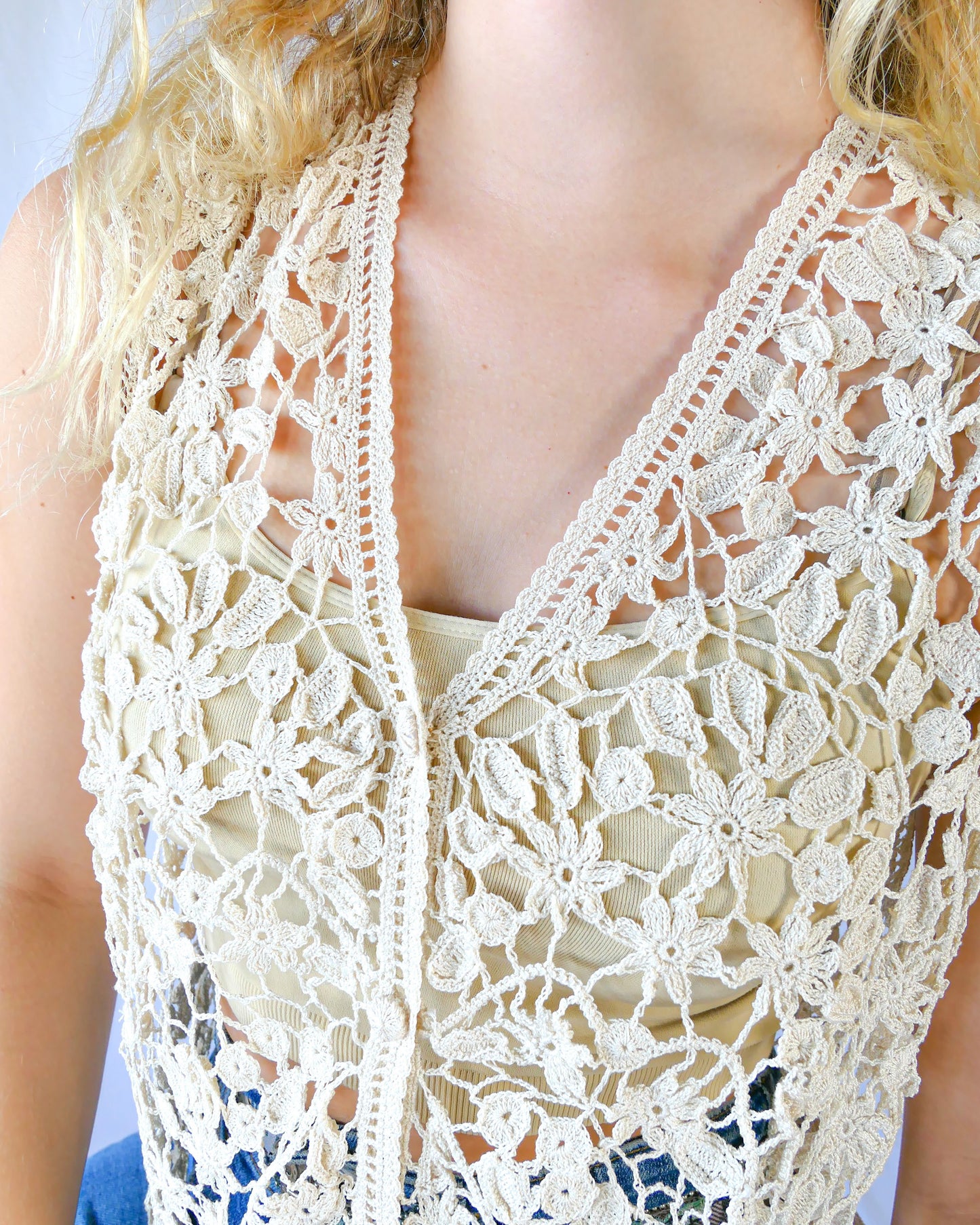 Closeup of natural colored vest. A Lim's Vintage original hand crocheted vest from the 1990s with a repeating jasmine floral and leaf motif throughout. Refined, delicate, and a vintage accent to your everyday wardrobe. Buttons up the front but can also be left open and worn over a bikini bra, tank top, or even a long sleeve shirt or blouse during cooler months. Due to the handmade nature of this vest, the length and bust circumference may vary slightly from piece to piece. 