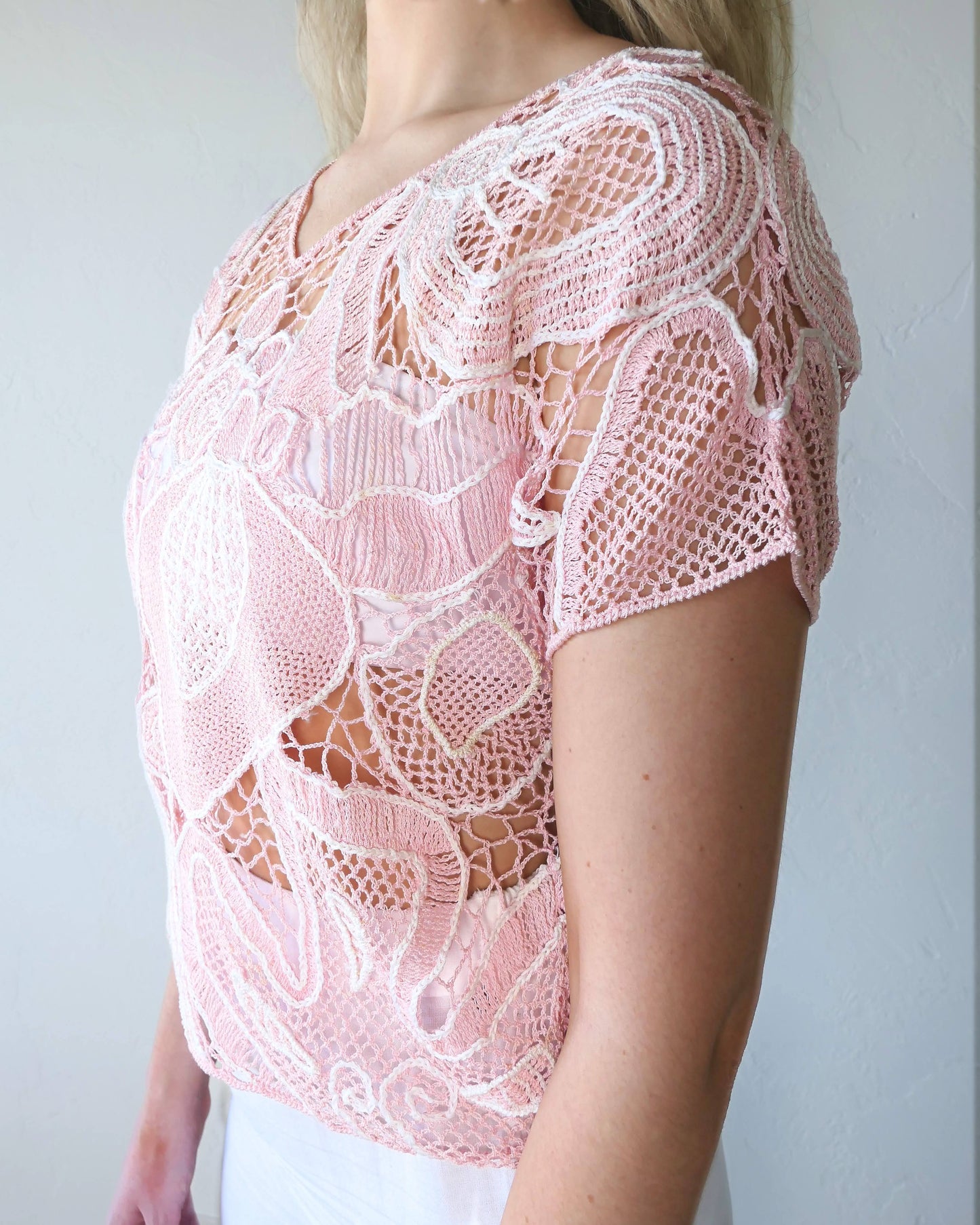 Close-up side view of girl wearing a crochet top with abstract flora design in colors of cotton candy pink and white. Lim's Vintage original crochet top from the 1980s.