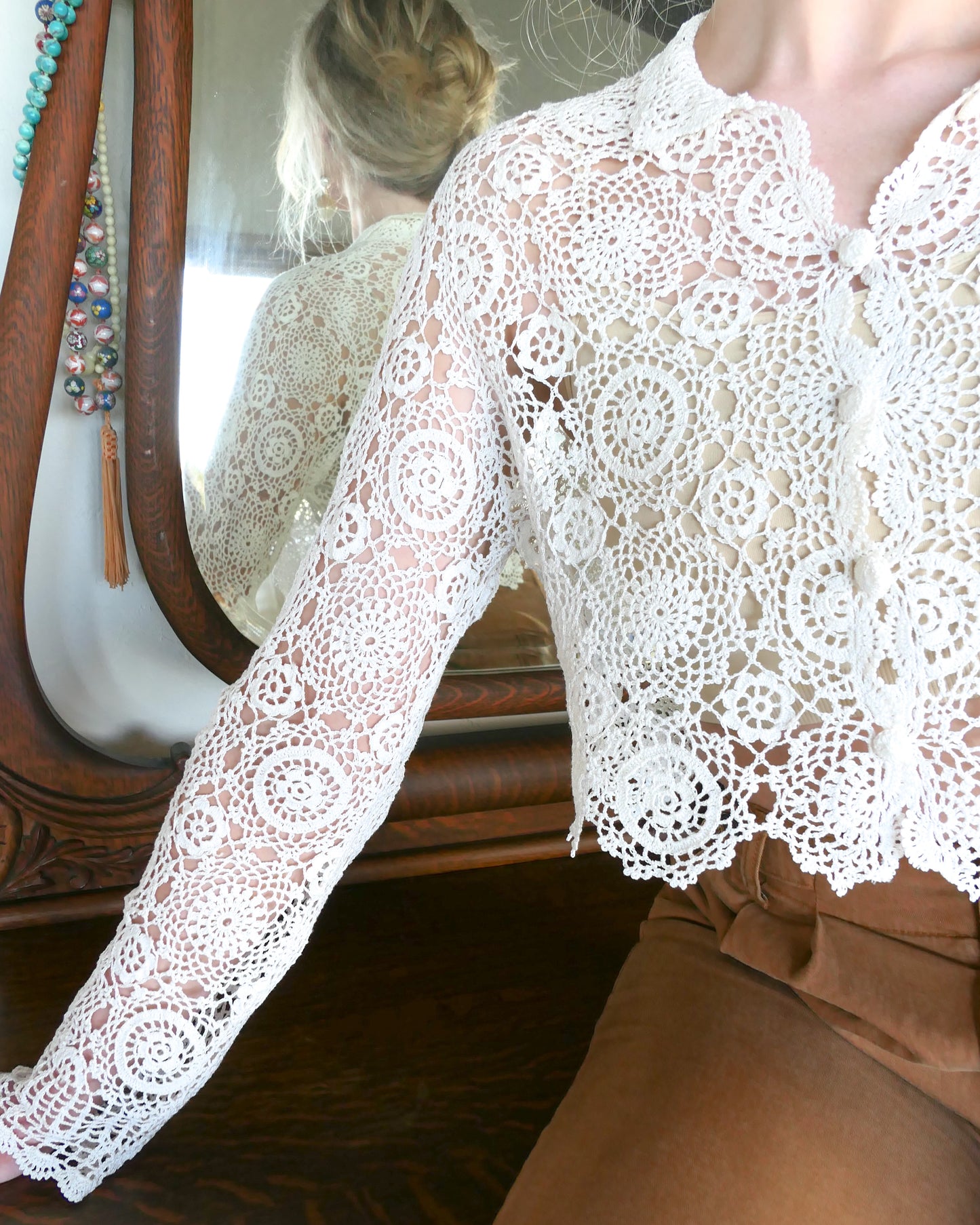 Closeup of sleeve. A versatile and boho chic hand crocheted cropped cardigan sweater in Ivory with a unique, repeating kaleidoscope-like floral pattern throughout. Dress it down with a pair of jeans and sandals, or dress it up with neutral colored wide leg pants, heels, and a pair of vintage dangly earrings.  Size: Fits Small to Medium