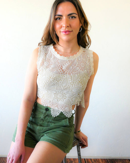 An ultra casual, hip, and boho-chic crop tank top made with interconnected flower doilies reminiscent of the white lotus, which symbolizes peace, tranquility, and calmness.  Lace trim at the collar and sleeve.  Model is wearing a natural colored crochet top. 
