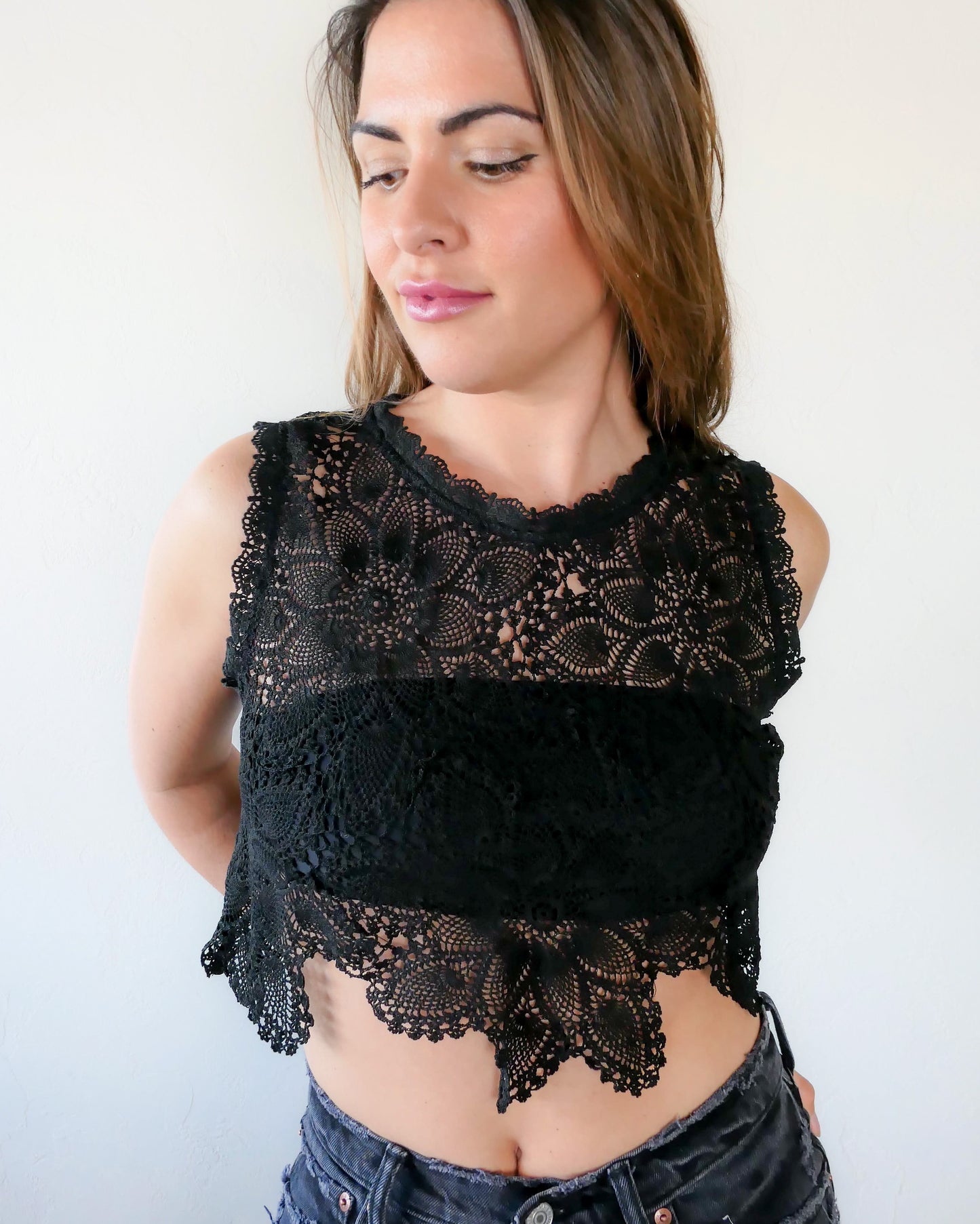 An ultra casual, hip, and boho-chic crop tank top made with interconnected flower doilies reminiscent of the white lotus, which symbolizes peace, tranquility, and calmness.  Lace trim at the collar and sleeve.  Model is wearing black colored top. 