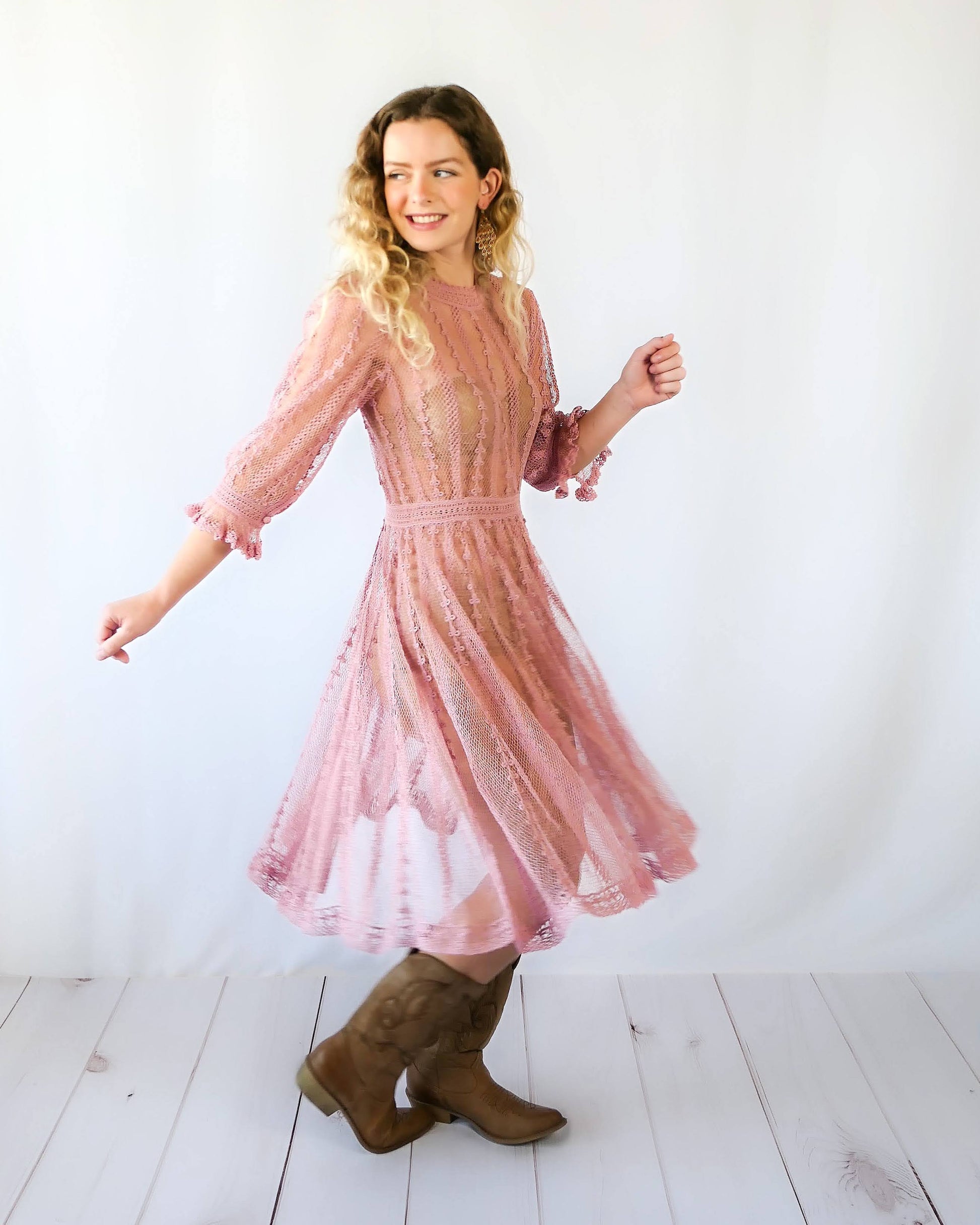 Picture of Lim's Vintage midi length crochet dress in muted rose color.  The model is twirling around.  Fitted waist, flares out towards the hem.  Ruffle at the bottom of the sleeves.  Made with fine cotton yarns to create a sheer look. 