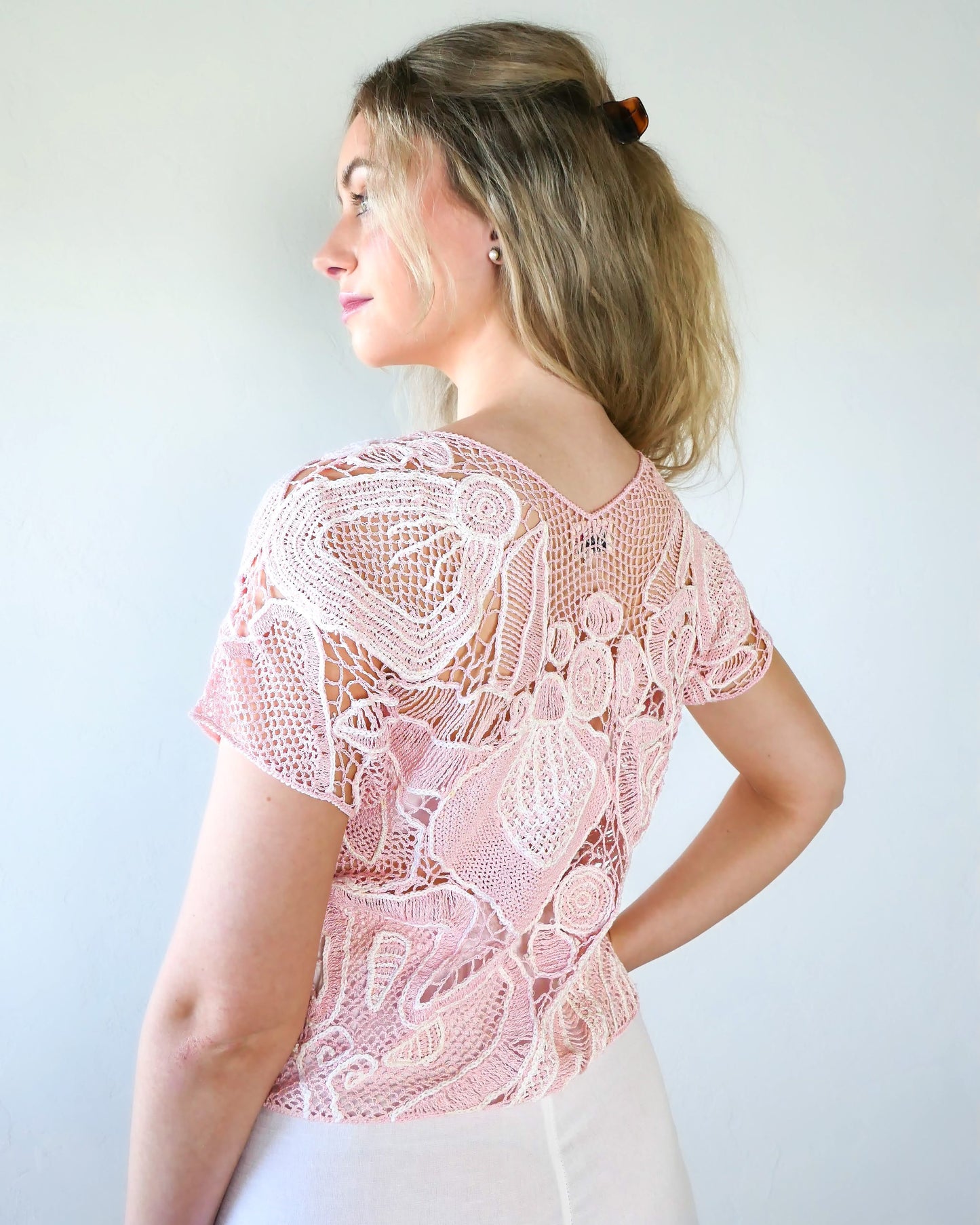 Back of view of girl wearing a crochet top with abstract flora design in colors of cotton candy pink and white. Lim's Vintage original crochet top from the 1980s. 