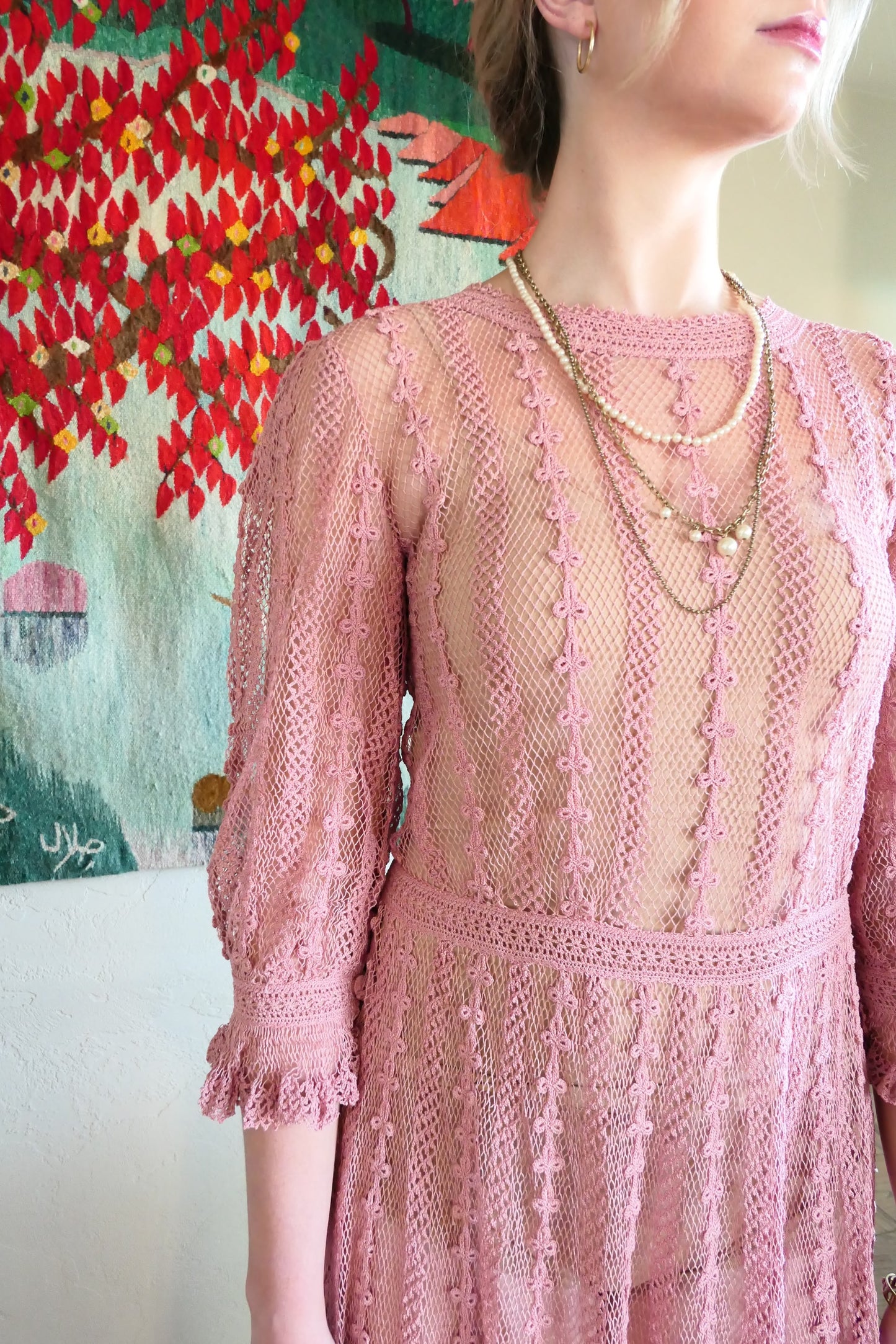 Closeup of top of dress.  One of our original Lim's crochet maxi dresses in a muted rose color from the 1980's. A darling of a piece and sure to turn heads, this dress was intricately hand crocheted using very fine cotton threads.   3/4 length sleeves, round collar, with ruffles at the wrist.  Model is wearing a natural colored slip underneath. 