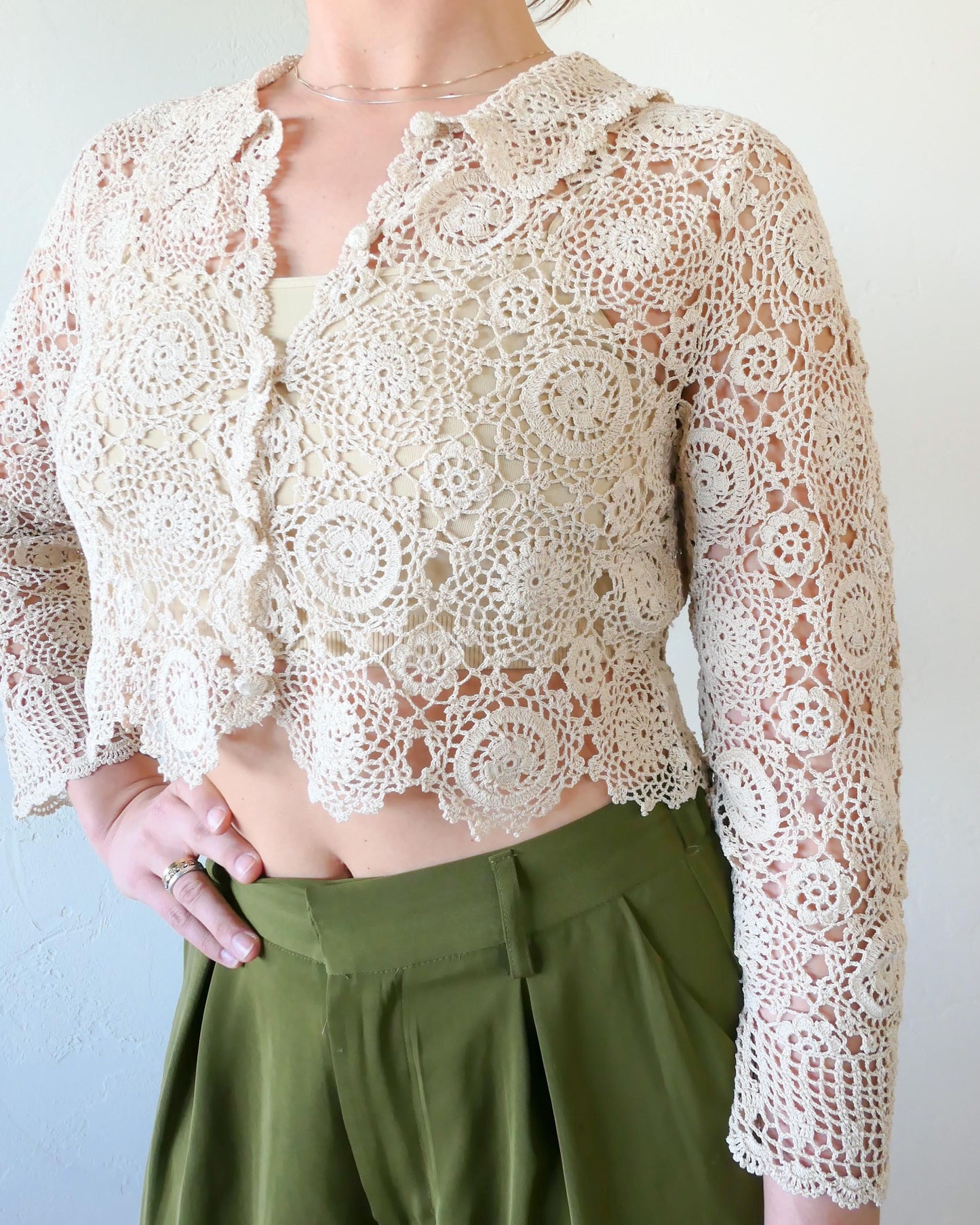 A versatile and boho chic hand crocheted cropped cardigan sweater with a unique, repeating kaleidoscope-like floral pattern throughout. Dress it down with a pair of jeans and sandals, or dress it up with neutral colored wide leg pants, heels, and a pair of vintage dangly earrings.