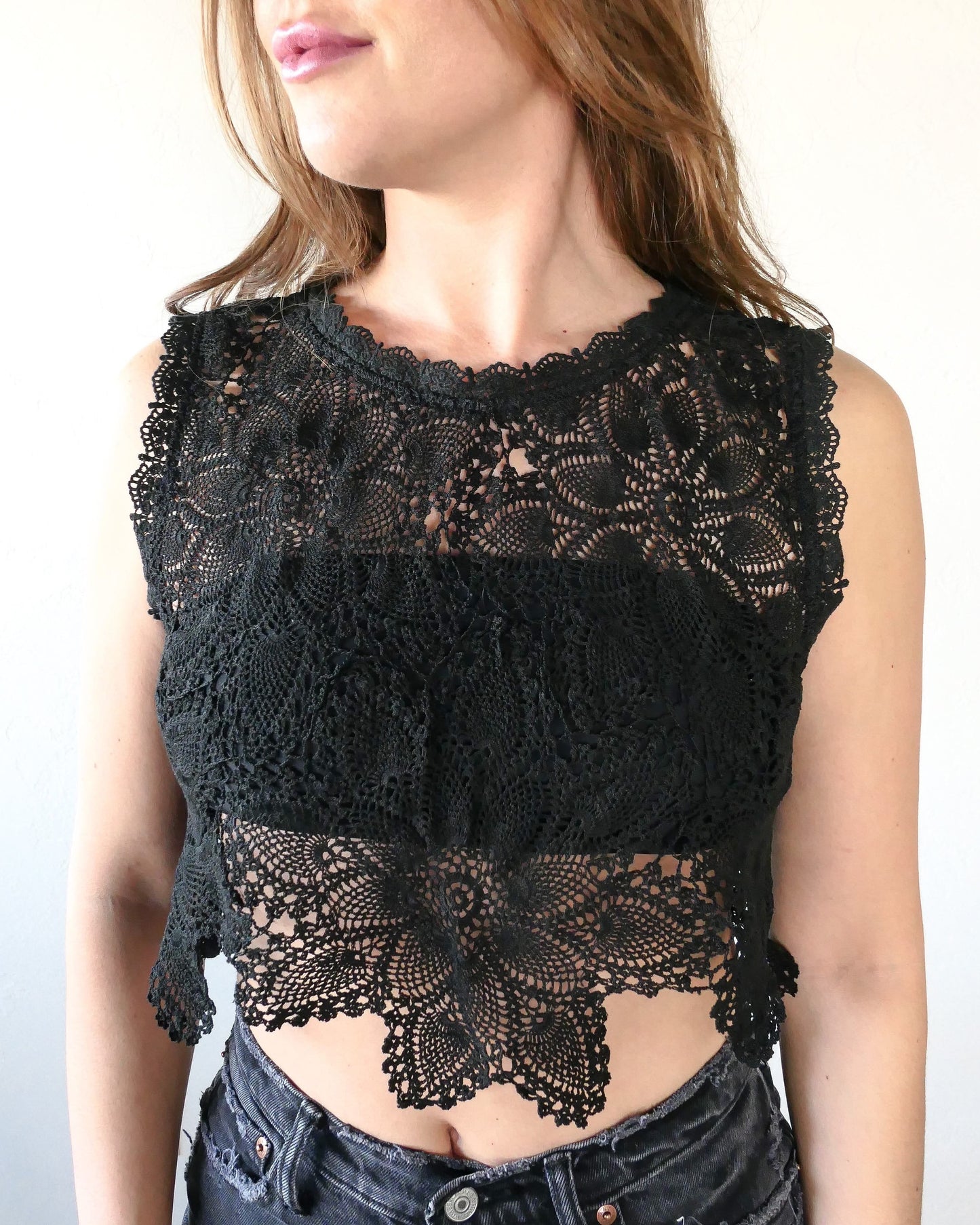 An ultra casual, hip, and boho-chic crop tank top made with interconnected flower doilies reminiscent of the white lotus, which symbolizes peace, tranquility, and calmness. Lace trim at the collar and sleeve. Model is wearing a black colored crochet Lim's Vintage top.