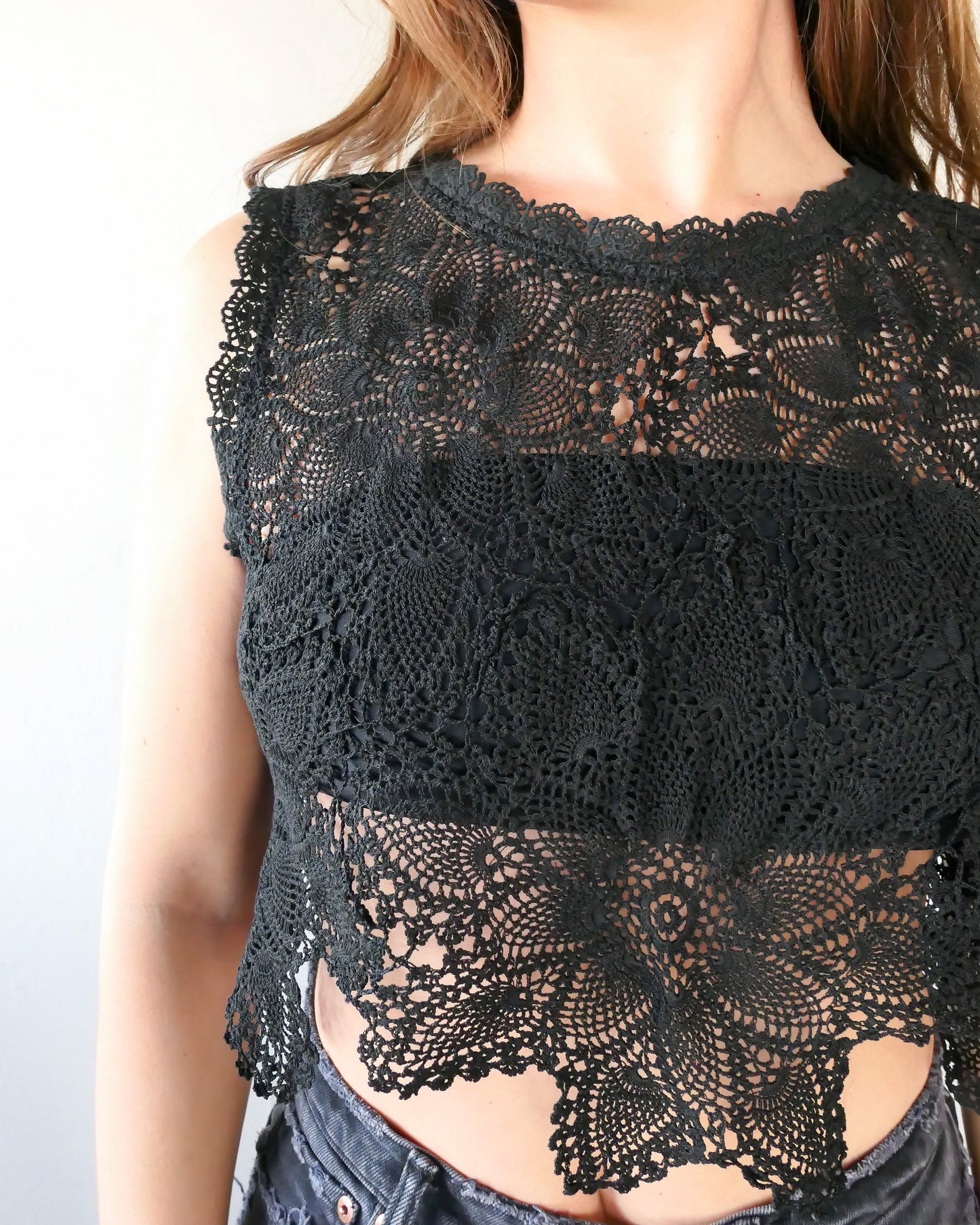 Closeup view of black crochet top. An ultra casual, hip, and boho-chic crop tank top made with interconnected flower doilies reminiscent of the white lotus, which symbolizes peace, tranquility, and calmness.  Lace trim at the collar and sleeve.  Model is wearing black colored top by Lim's Vintage.