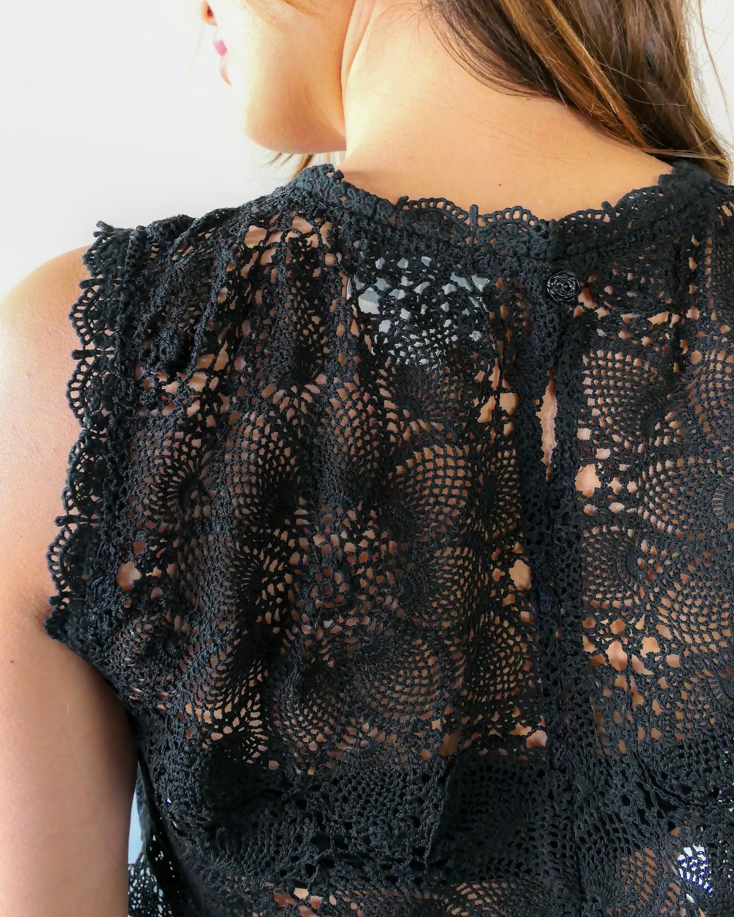 Closeup view of back of top. An ultra casual, hip, and boho-chic crop tank top made with interconnected flower doilies reminiscent of the white lotus, which symbolizes peace, tranquility, and calmness.  Lace trim at the collar and sleeve.  Model is wearing black colored top by Lim's Vintage. 
