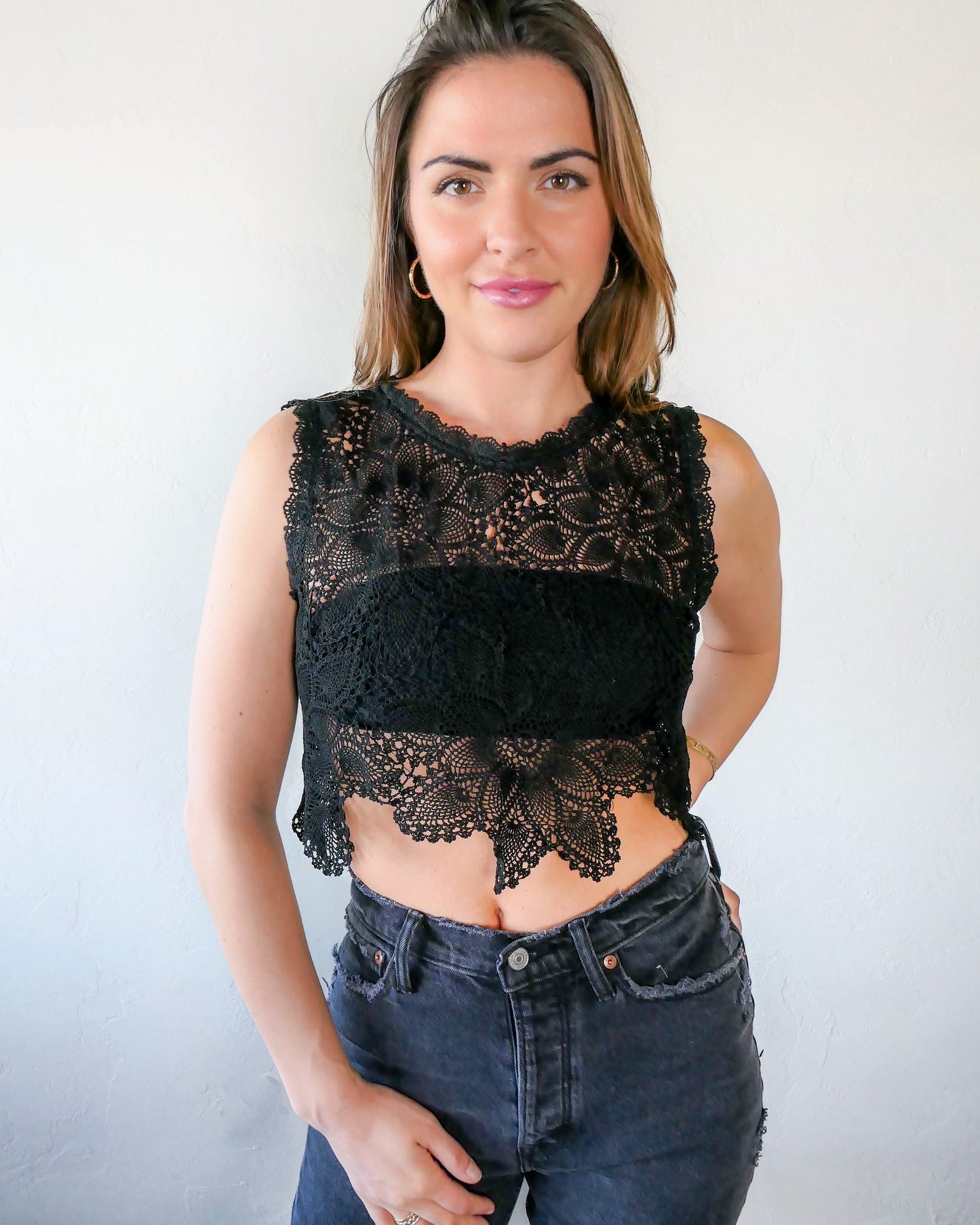 An ultra casual, hip, and boho-chic crop tank top made with interconnected flower doilies reminiscent of the white lotus, which symbolizes peace, tranquility, and calmness.  Lace trim at the collar and sleeve.  Model is wearing black colored crochet top. 
