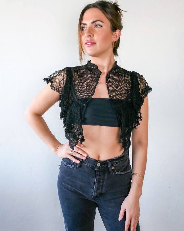 A super cool, super sassy hand crocheted fitted crop top in black with plenty of ruffles and frills for a fun, vintage inspired wardrobe.  Buttons up the front and crochet ruffles along the front covering the chest and over the shoulders.  The model is wearing this top unbuttoned. 