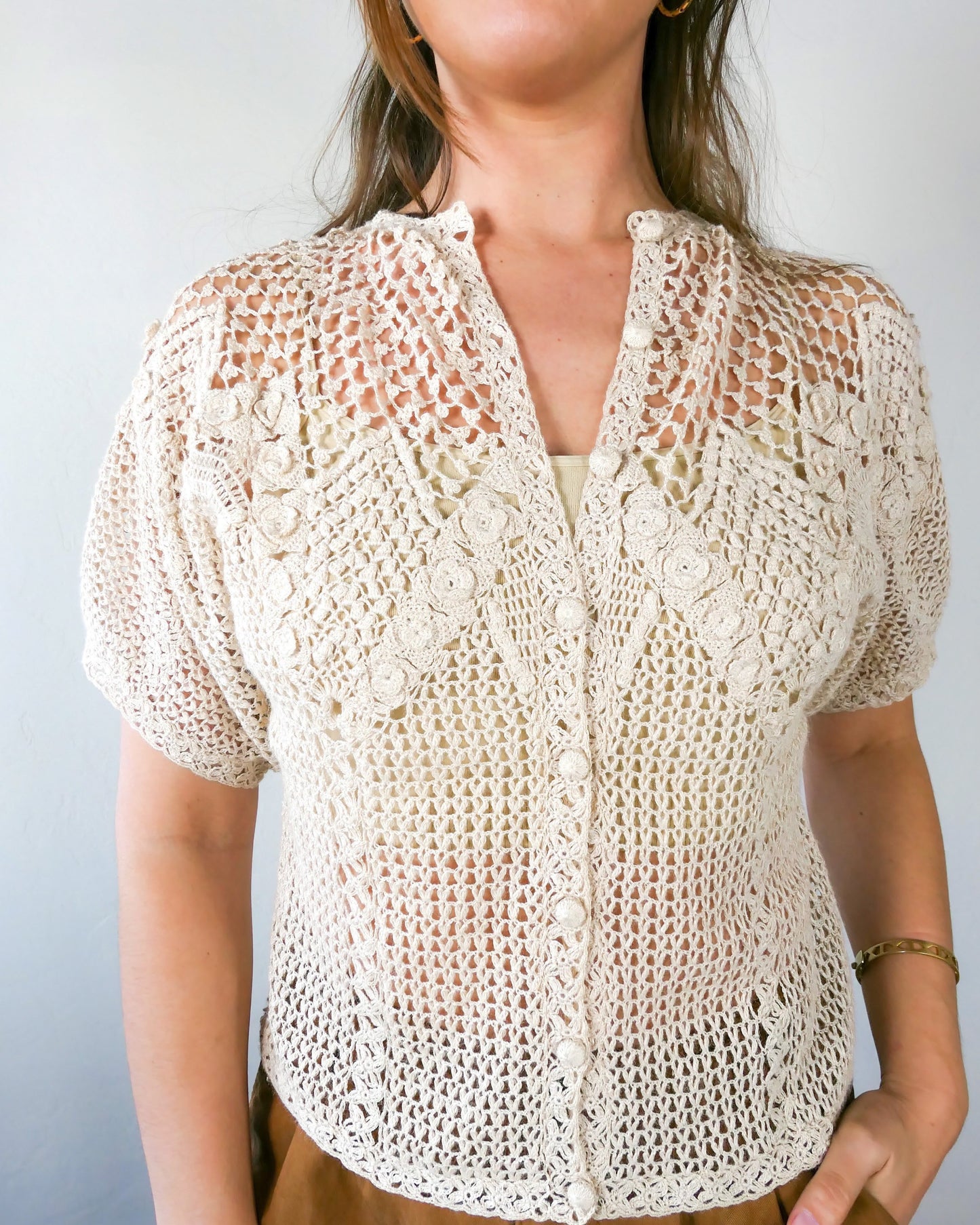 Closeup of top. A classic Lim's Vintage hand crocheted button down top with a beautiful zig zag pattern on both the front and back, with lighter stitching around the chest and shoulders to bring a sense of lightness and space to the neckline. Petite flower buds sprout up from and accent the edges of the zig zag. This natural color top is versatile, comfortable, and adds a beautiful vintage accent to your wardrobe.