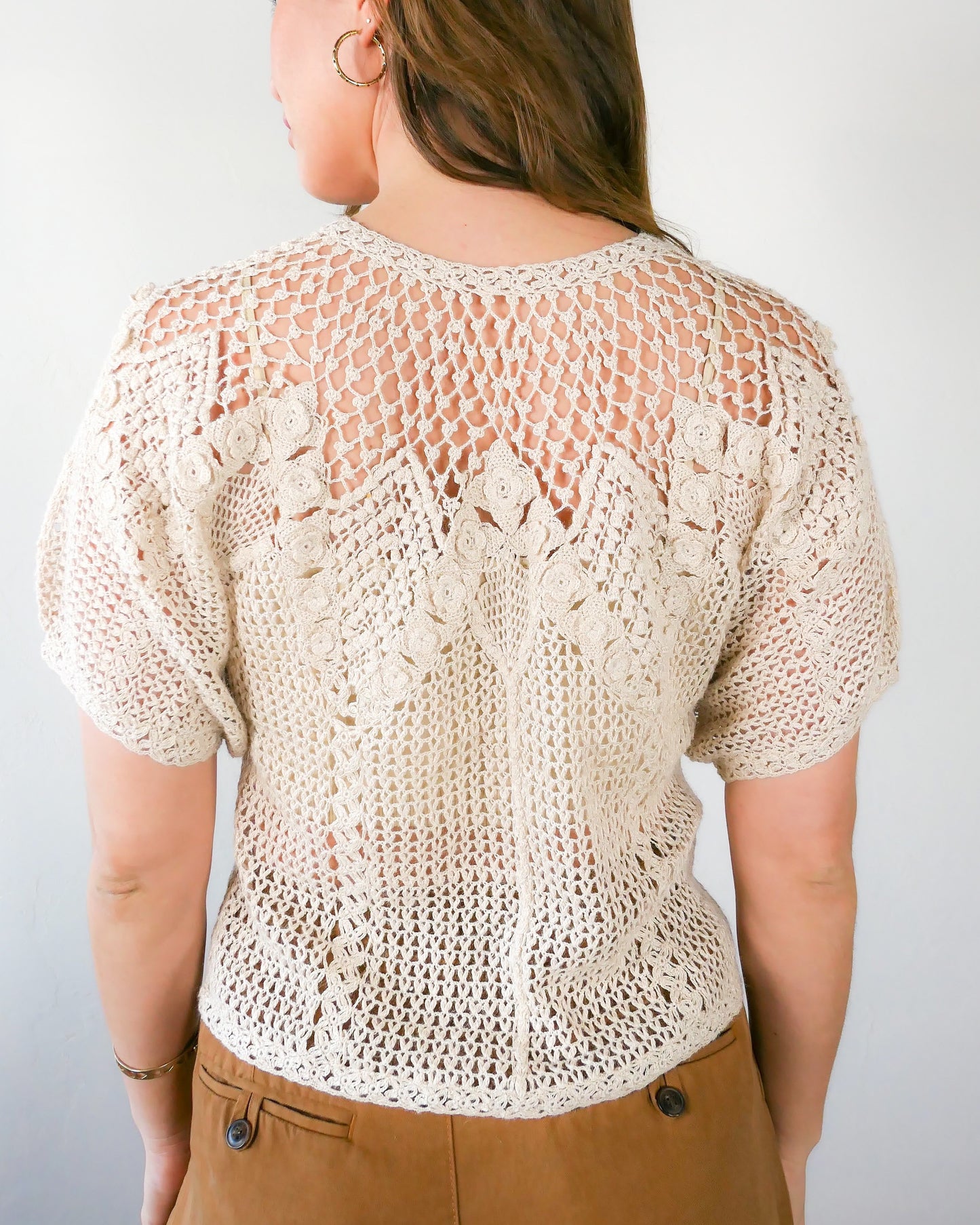 View of back of top with no buttons. A classic Lim's Vintage hand crocheted button down top with a beautiful zig zag pattern on both the front and back, with lighter stitching around the chest and shoulders to bring a sense of lightness and space to the neckline. Petite flower buds sprout up from and accent the edges of the zig zag. This natural color top is versatile, comfortable, and adds a beautiful vintage accent to your wardrobe.