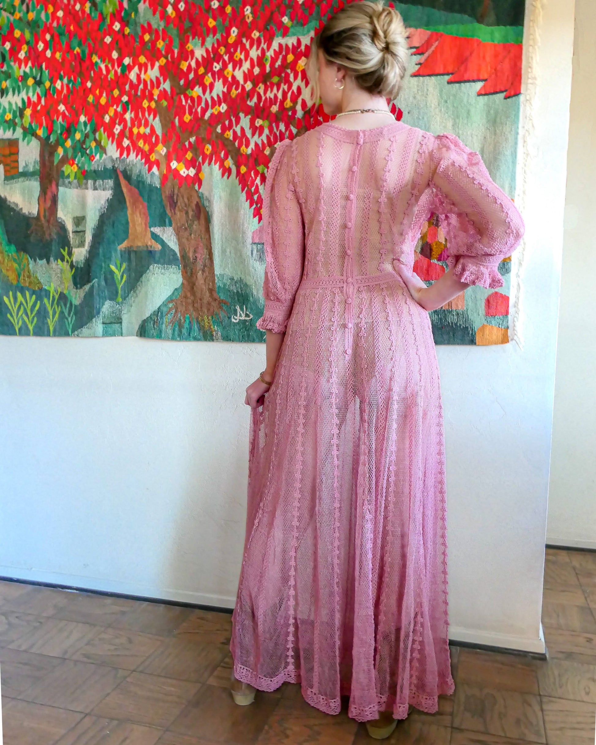Back view of dress. One of our original Lim's crochet maxi dresses in a muted rose color from the 1980's. A darling of a piece and sure to turn heads, this dress was intricately hand crocheted using very fine cotton threads.   3/4 length sleeves, round collar, with ruffles at the wrist.  Model is wearing a natural colored slip underneath. 