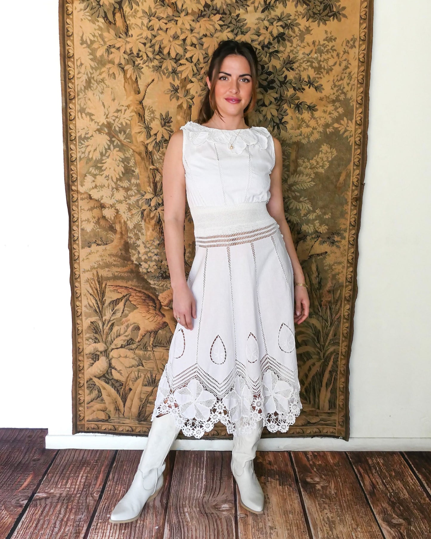 A white cotton midi dress with whimsical crochet and embroidered flowers at the hem and collar, and teardrop shaped eyelet detail on the skirt. Stretchable ribbed knit fabric around the waist adds contour to the dress.  Made by Lim's Vintage.