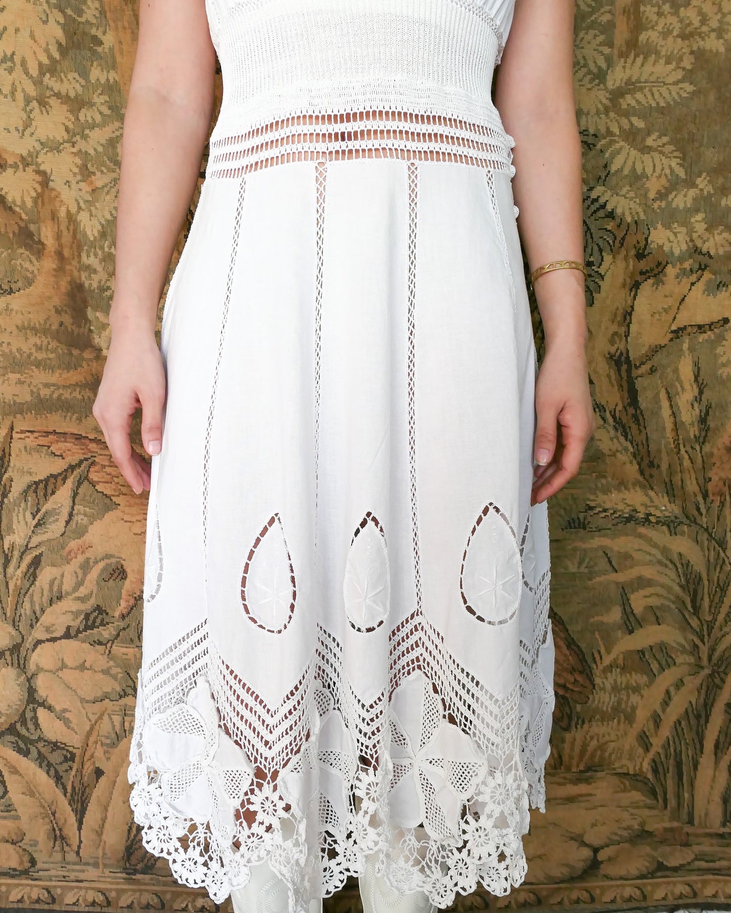 A white cotton midi dress with whimsical crochet and embroidered flowers at the hem and collar, and teardrop shaped eyelet detail on the skirt. Stretchable ribbed knit fabric around the waist adds contour to the dress. By Lim's Vintage