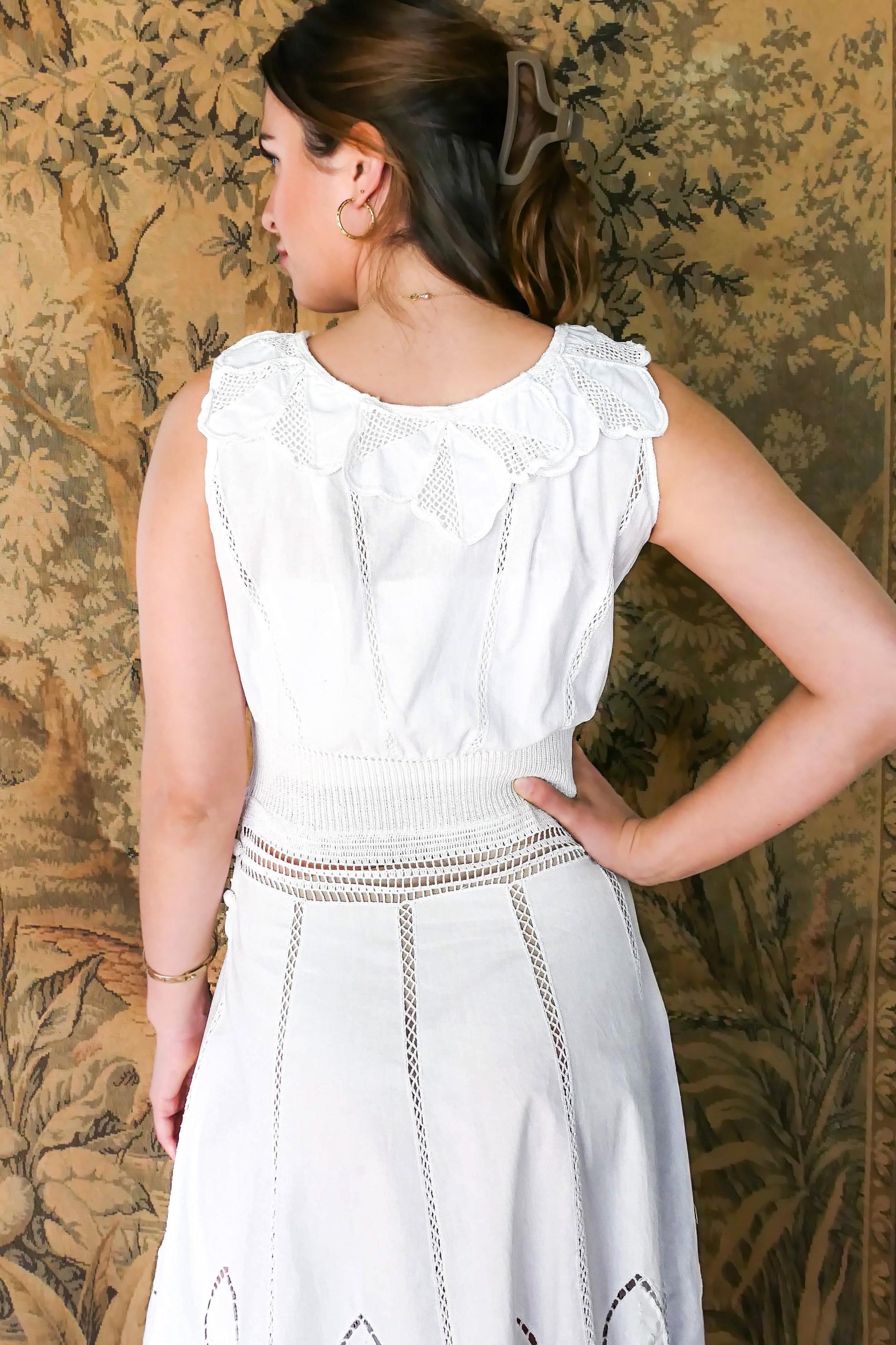 Closeup view of back of dress with floral inspired collar.  A white cotton midi dress with whimsical crochet and embroidered flowers at the hem and collar, and teardrop shaped eyelet detail on the skirt. Stretchable ribbed knit fabric around the waist adds contour to the dress.