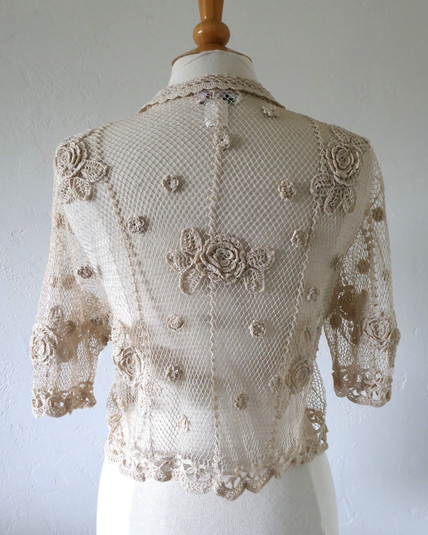 Lim's VIntage natural colored cropped crochet cardigan with carnation floral motif, notched collar, and scalloped edging around sleeve hem and bottom hem.  Back view. One size.