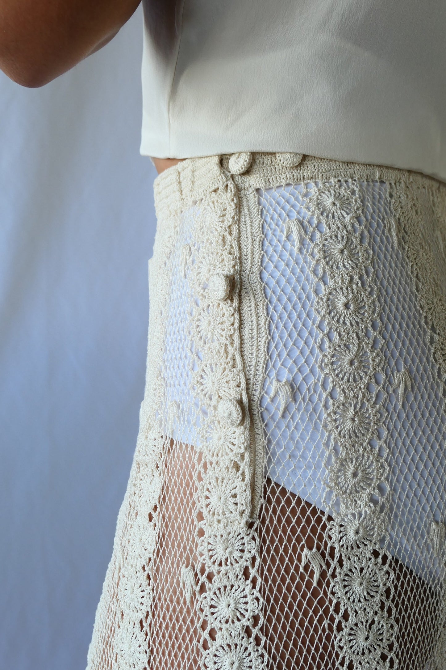 This Lim's Vintage crochet skirt is made with very fine threads to form a delicate net-like pattern throughout, coupled with vertical stripes made of linking pinwheel shaped circles, and a floral motif hem. The skirt is slightly stretchable and comes with a comfortable elastic waistband and buttons up one side of the waist.