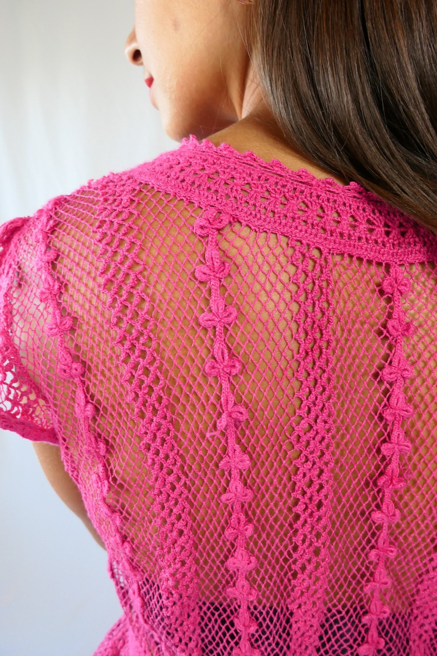 close-up view of back.  Delicate mesh pattern hand crocheted short puff sleeve top in a pretty fuschia pink!  This top has a high waist and flared hem. This is a Lim’s original vintage piece from the 1980s with trim added recently to finish the hem.  The top is reversible and can be buttoned up the front or back.  