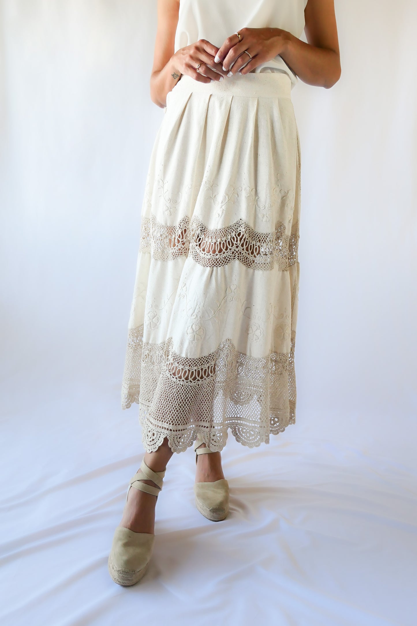 Picture yourself strolling through a sunlit Mediterranean village in this beautiful raw silk maxi skirt - an original Lim's skirt from the 1990s - with hand embroidered floral embellishments and hand crocheted trim.  This skirt has a fitted, non-elastic waistband and is semi-pleated at the waist with three crochet buttons going up the side of the skirt.  Measurements:  Fits a size XS to Small Waist 26" Skirt length 33", hip 50"  Color: Natural Material: Raw silk and cotton