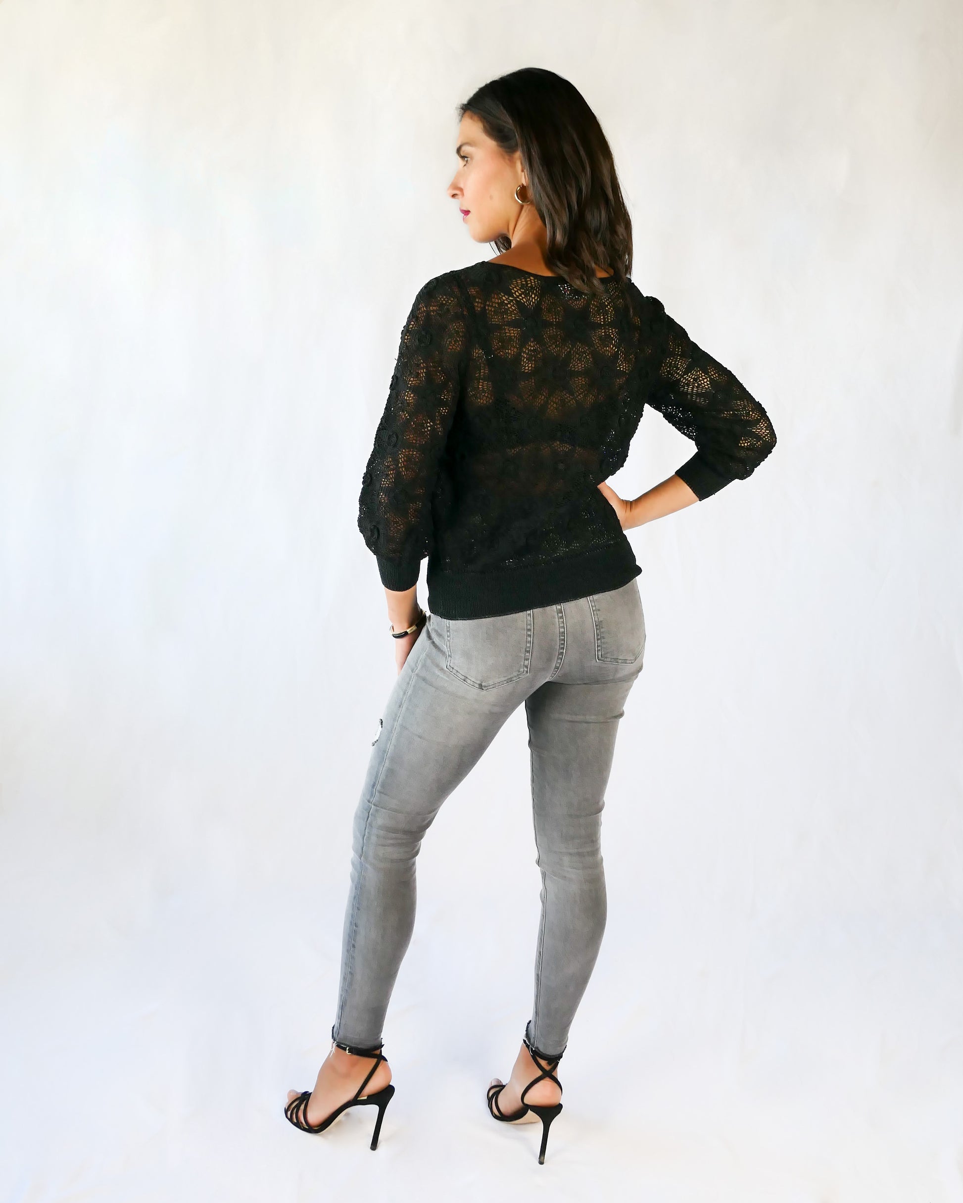 Back view. Your everyday fitted sweater with a twist. A Lim's Vintage original hand crocheted crewneck sweater in basic black with star shaped flowers and elastic banding at the hip and wrists.