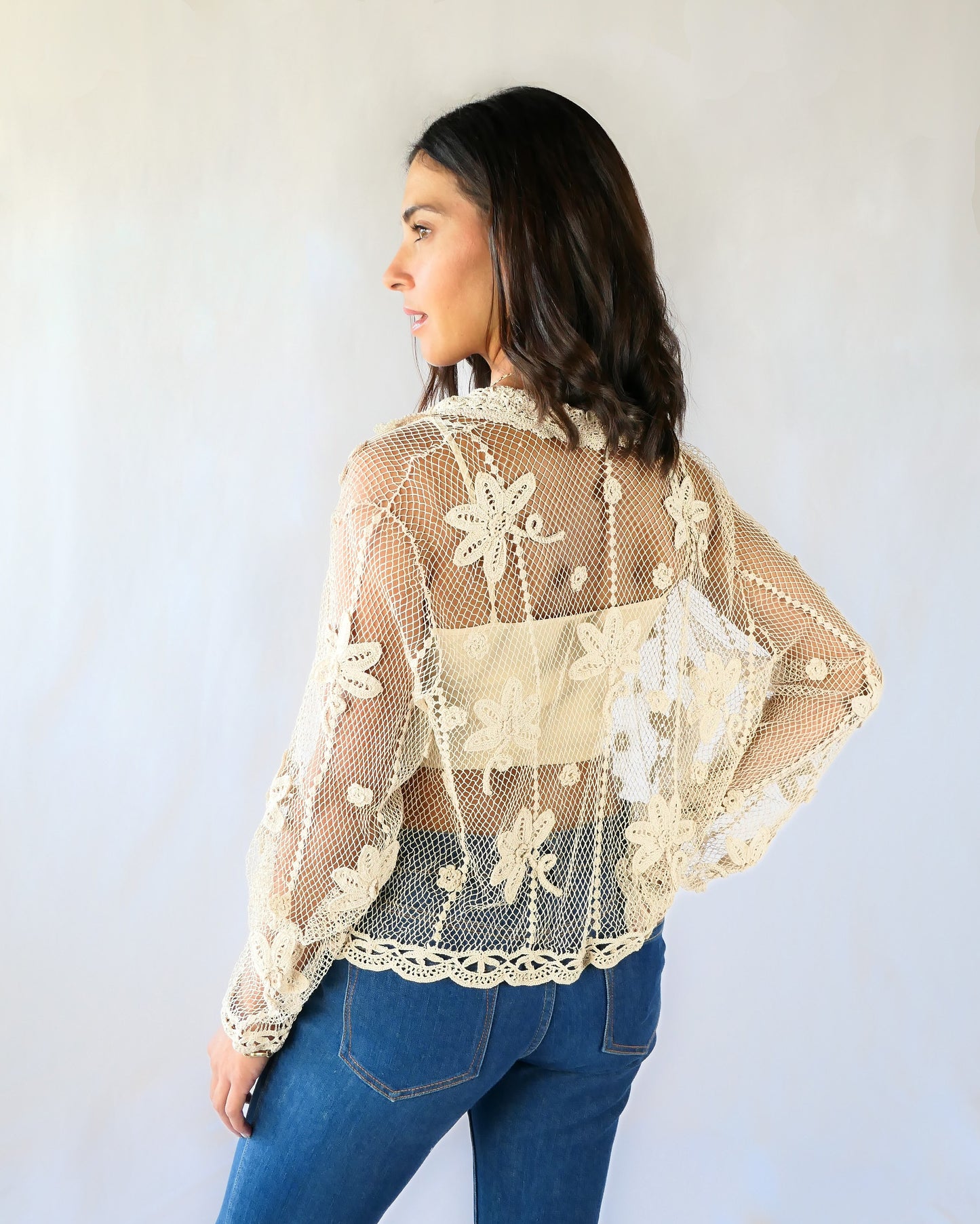 Back view of cardigan. A sheer, hand crocheted Lim's Vintage original long sleeve cardigan with a wide notched collar and daisy floral motif design throughout. Pair it with a tank top, jeans, and boots or sandals for a fresh, boho chic look.