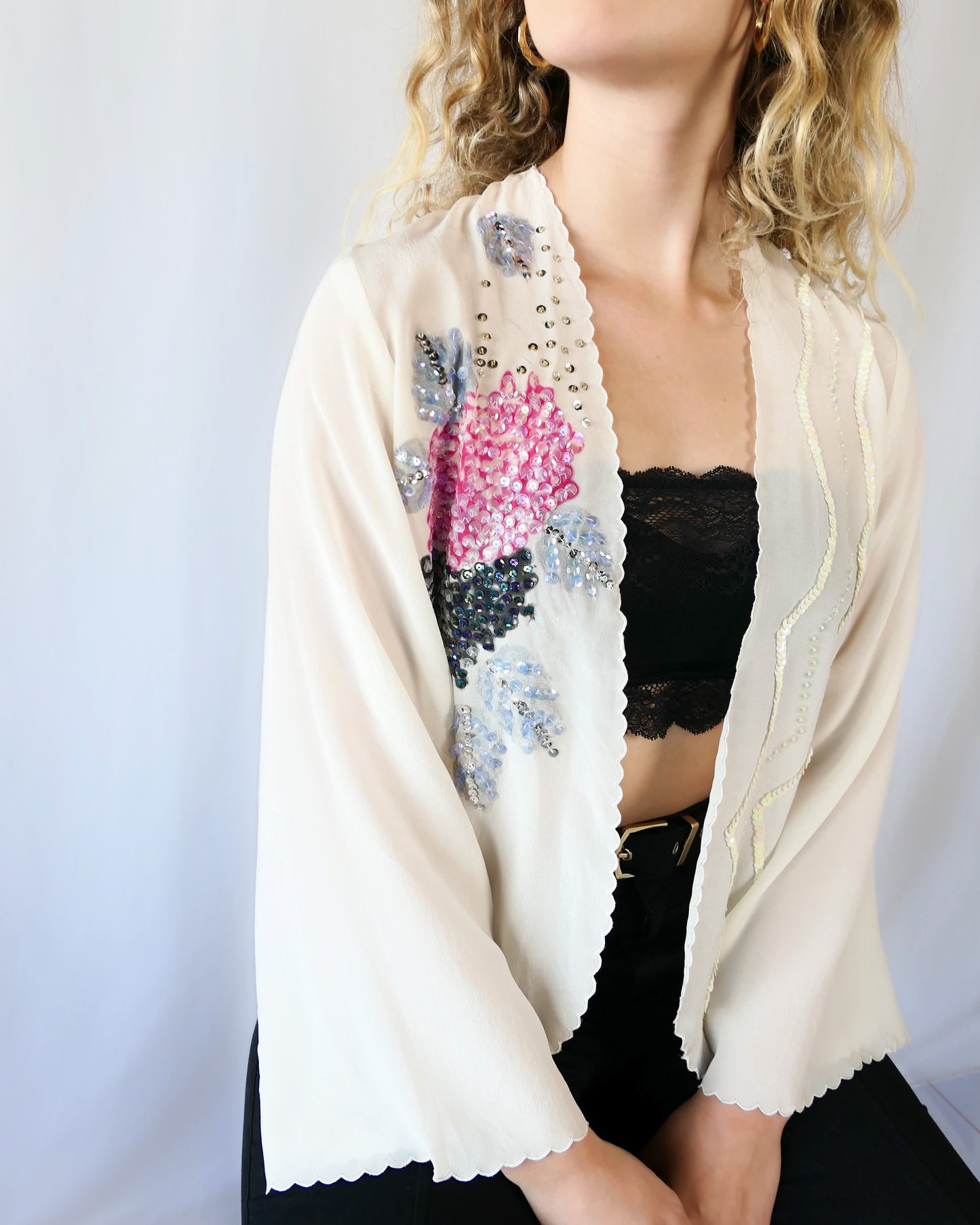From Lim's Vintage: An elegant hand painted silk kimono top that drapes over effortlessly, with a relaxed fit and elegent scalloped edging along the borders and sleeve hem. Hand painted pink peony flowers and muted lavender grey and black foliage are adorned with iridescent and silver sequins. One size fits most. Size: One Size Measurements: Bust 42” Waist 41" Length 24” Shoulder width 15” Sleeve 20.5” Color: Ivory Material: 100% silk with plastic sequins