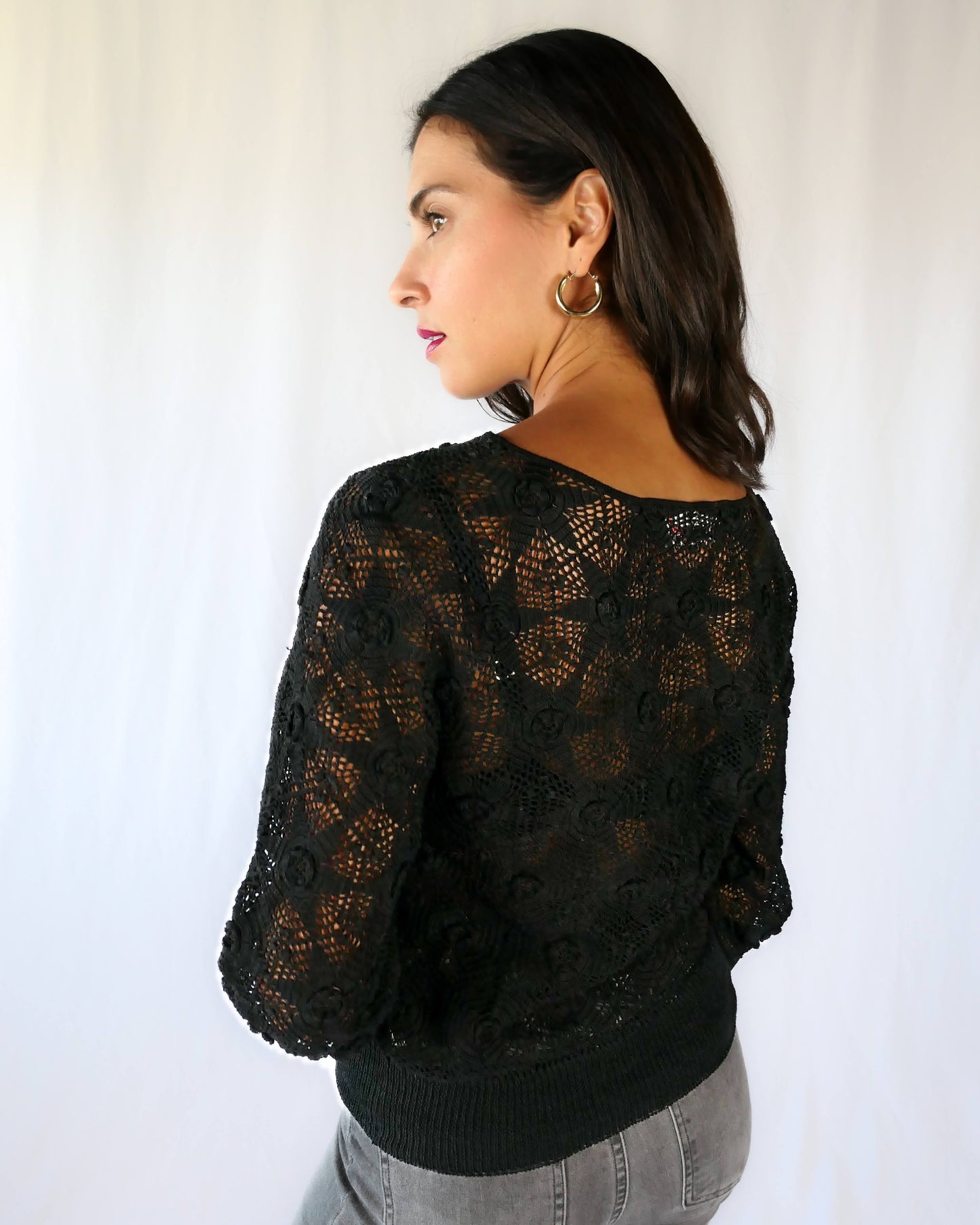 Close-up of back view. Your everyday fitted sweater with a twist. A Lim's Vintage original hand crocheted crewneck sweater in basic black with star shaped flowers and elastic banding at the hip and wrists.
