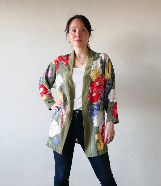 A hand painted silk kimono jacket of vibrant colored flowers dotted with gold and purple sequins  amidst a backdrop of olive green dyed and salted silk. Salting creates a unique pattern on the jacket reminiscent of ripples of water on a lake, which lends a feeling of both texture and depth. One size fits most. We have only one of these original Lim's pieces in stock! Wear it with jeans for a casual date, or dress it up with heels for an evening out.