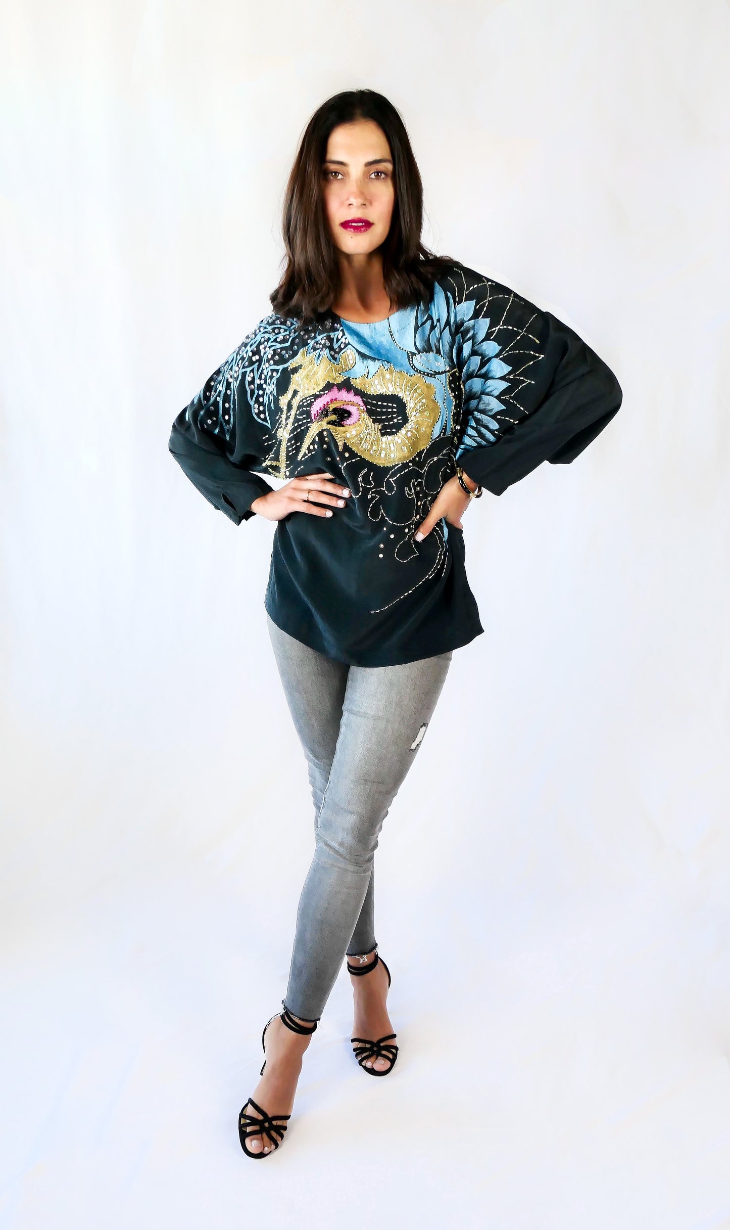 Make a bold party statement in this black silk pullover top with a hand-painted gold and turquoise phoenix, embellished with iridescent, pink, black, and clear colored sequins. In Chinese culture, the phoenix is a symbol of virtue, harmony, balance and peace. This beautifully made top is sure to bring harmony to your wardrobe as well!