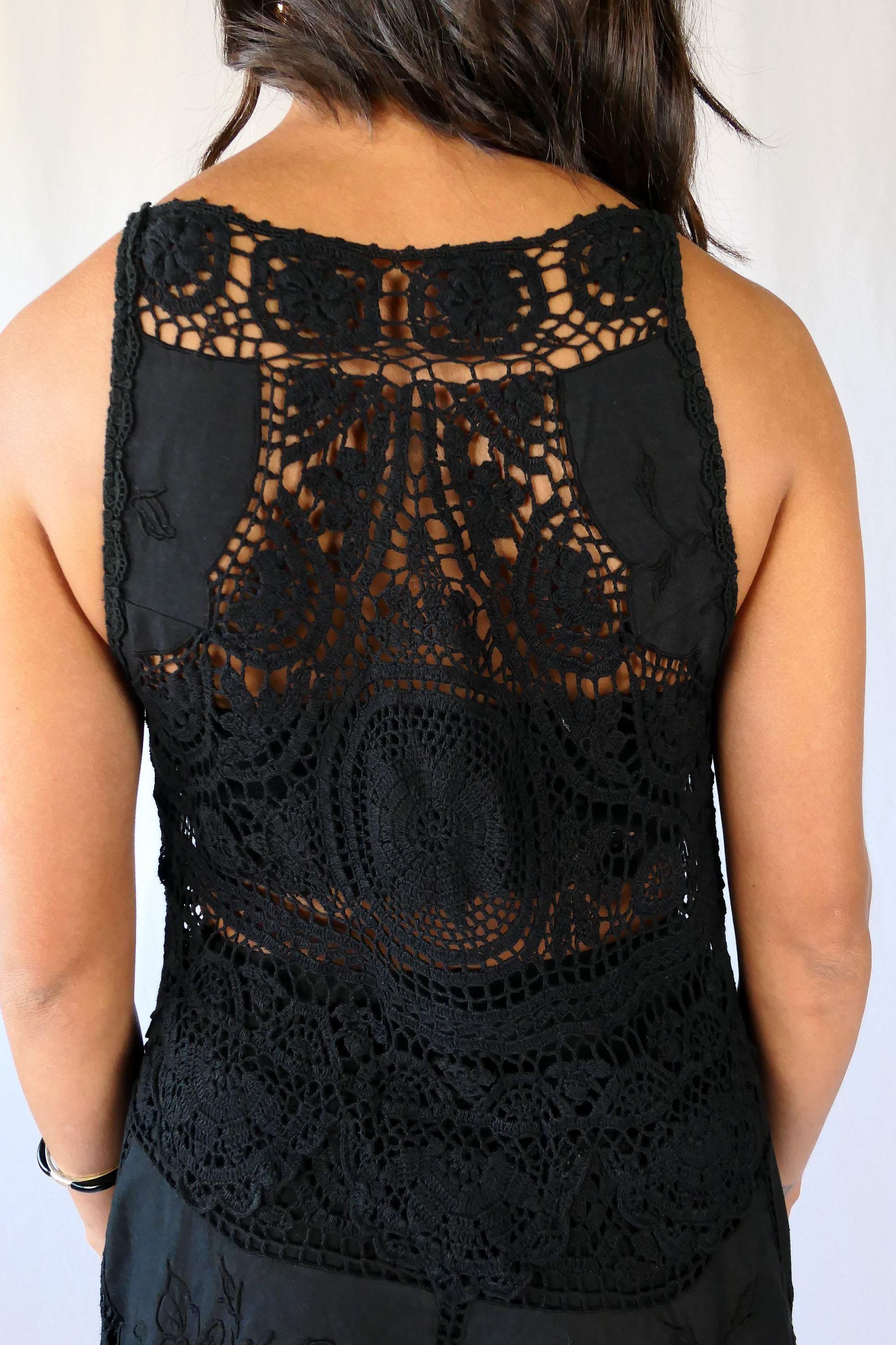 Close-up of the back. This Little Black Dress with detailed hand crochet and embroidery work lends itself a vintage flair.  The dress can be buttoned up the front or back, has a flattering fit at the waist, and flares out towards the hem.  Wear it as a cocktail dress with black heels or sandals, or as a beach coverup.  