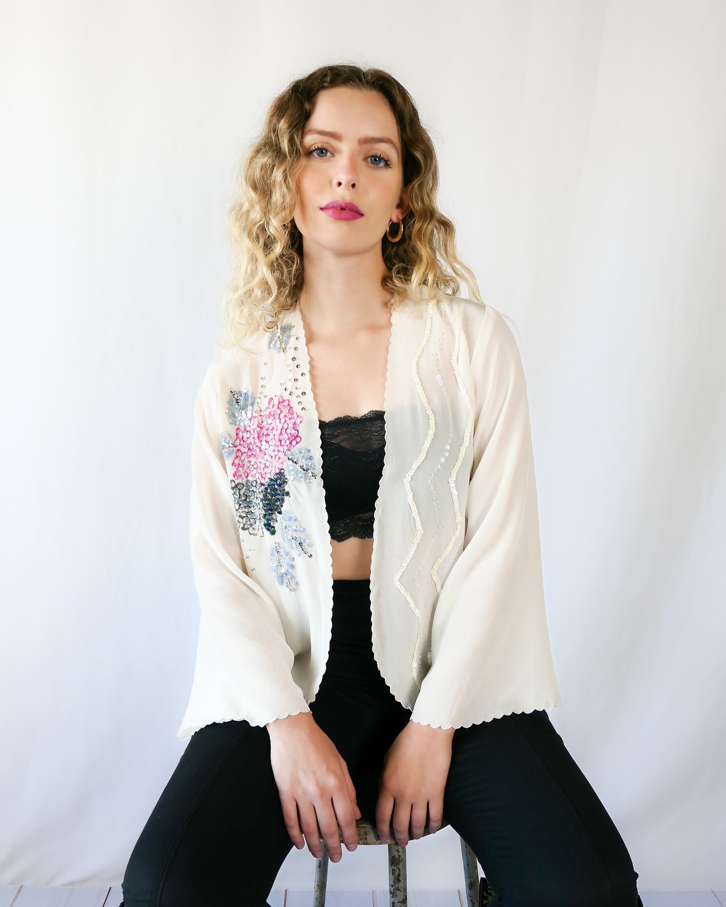 From Lim's Vintage: An elegant hand painted silk kimono top that drapes over effortlessly, with a relaxed fit and elegent scalloped edging along the borders and sleeve hem. Hand painted pink peony flowers and muted lavender grey and black foliage are adorned with iridescent and silver sequins.  One size fits most.  Size: One Size   Measurements:  Bust 42” Waist 41" Length 24” Shoulder width 15” Sleeve 20.5” Color: Ivory   Material: 100% silk with plastic sequins