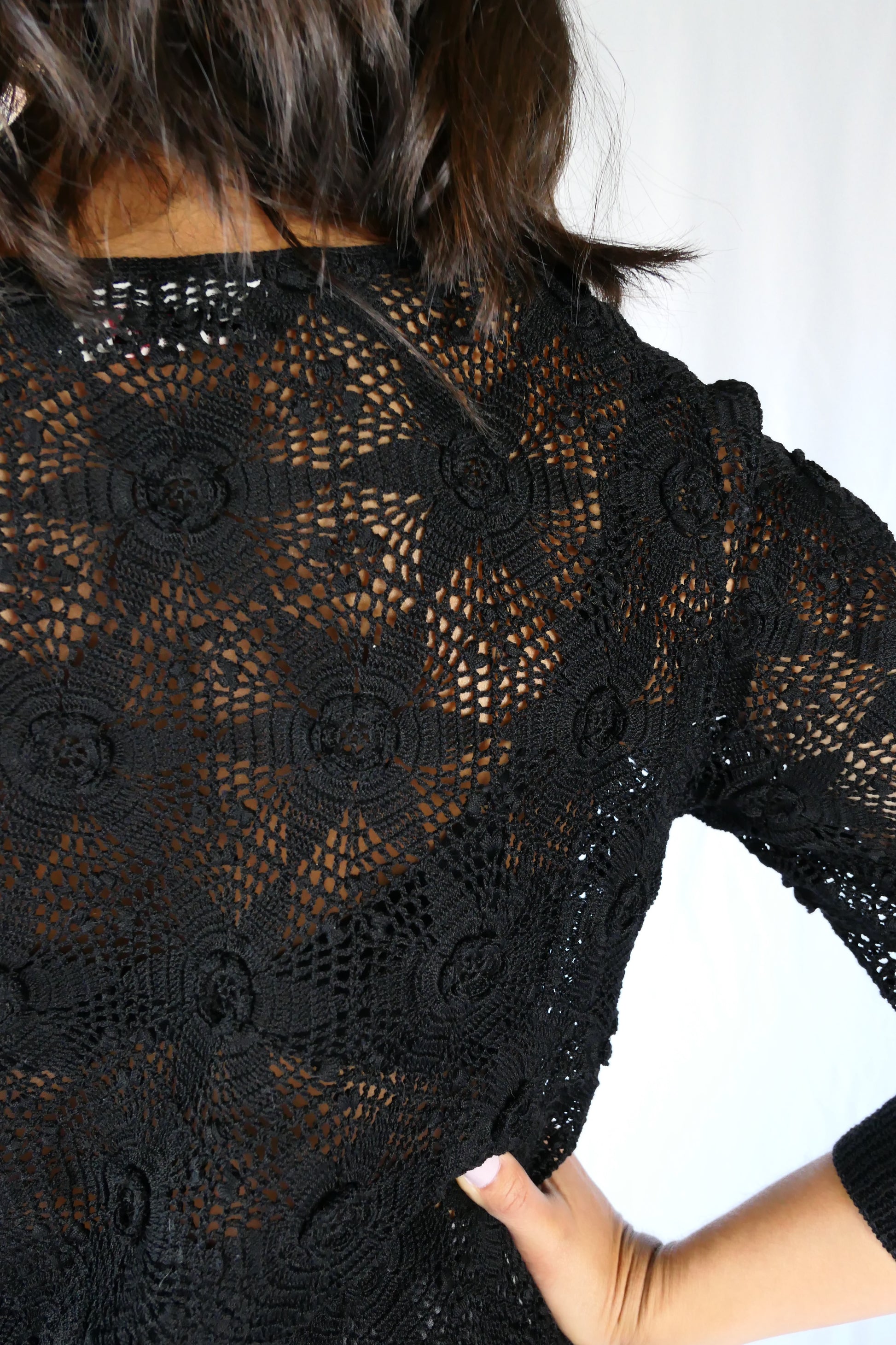 Close-up of detail. Your everyday fitted sweater with a twist. A Lim's Vintage original hand crocheted crewneck sweater in basic black with star shaped flowers and elastic banding at the hip and wrists.